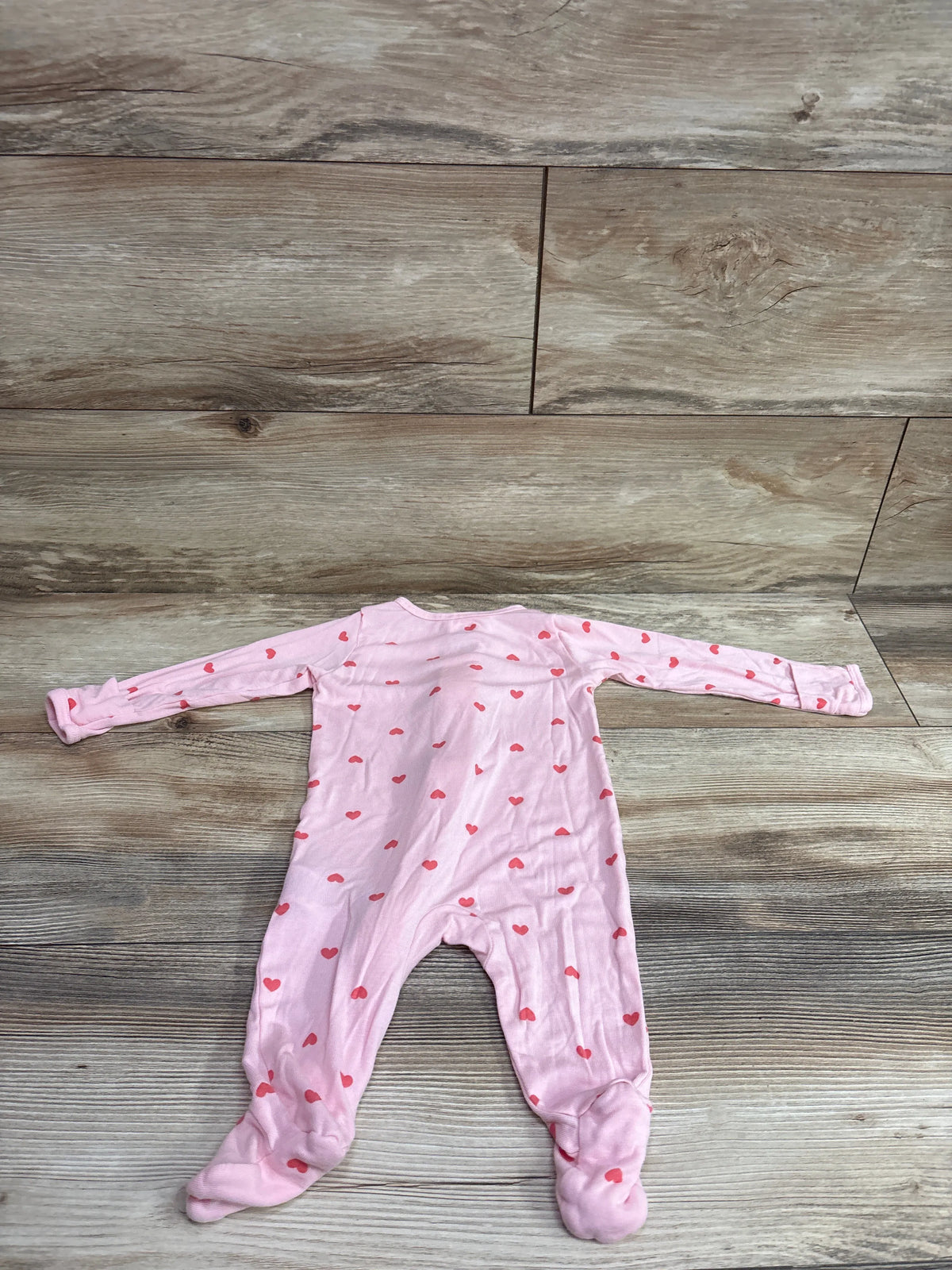 Flat lay of a pink heart-print baby sleeper showcasing long sleeves and footed legs on a wood-look background