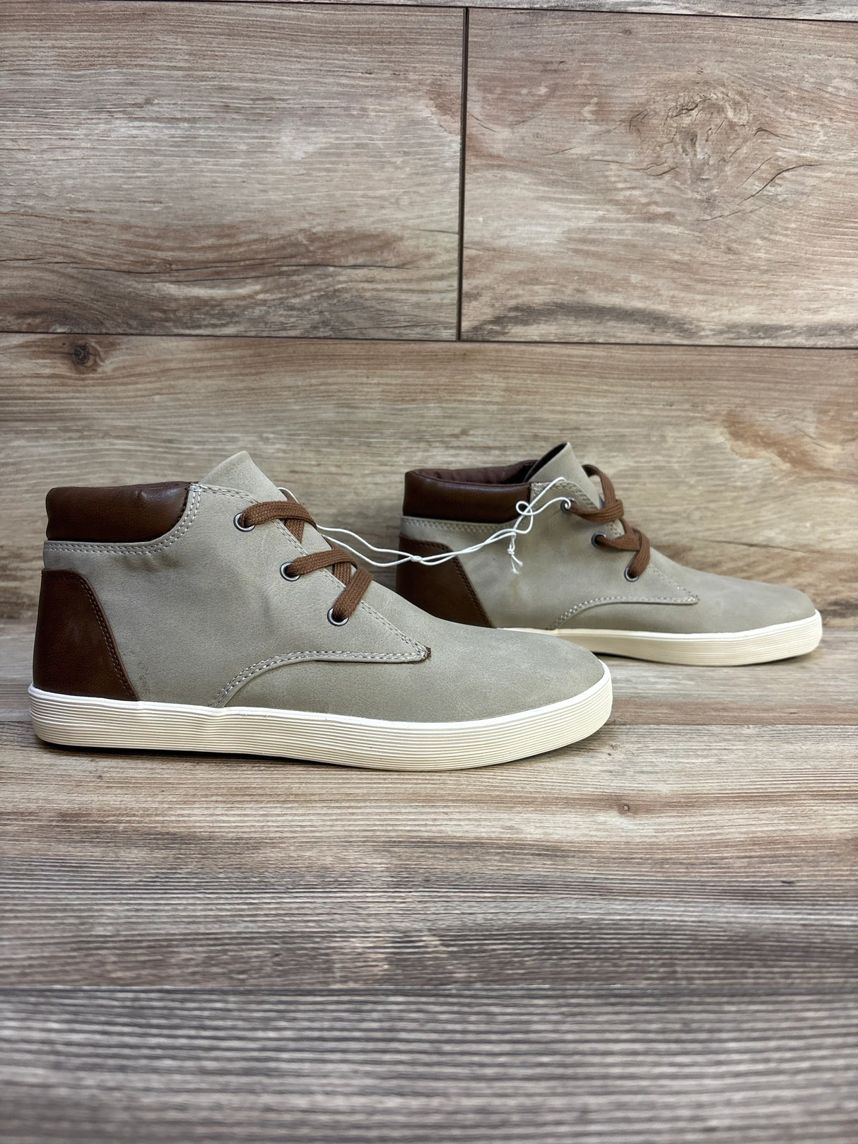 Kids tan high-top sneakers with brown accents and white soles on wood floor
