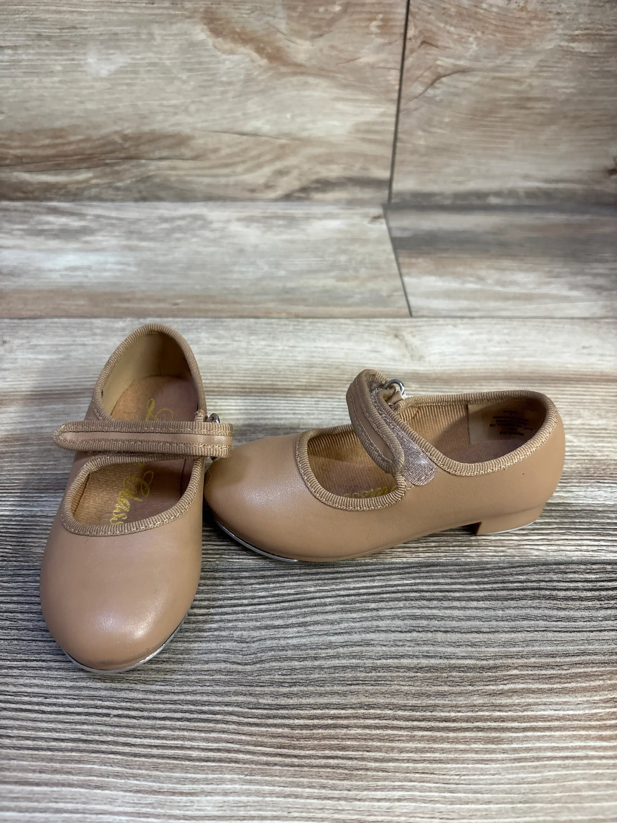 Front and side view of tan tap shoes in size 7C showcasing adjustable straps on a wood-look background