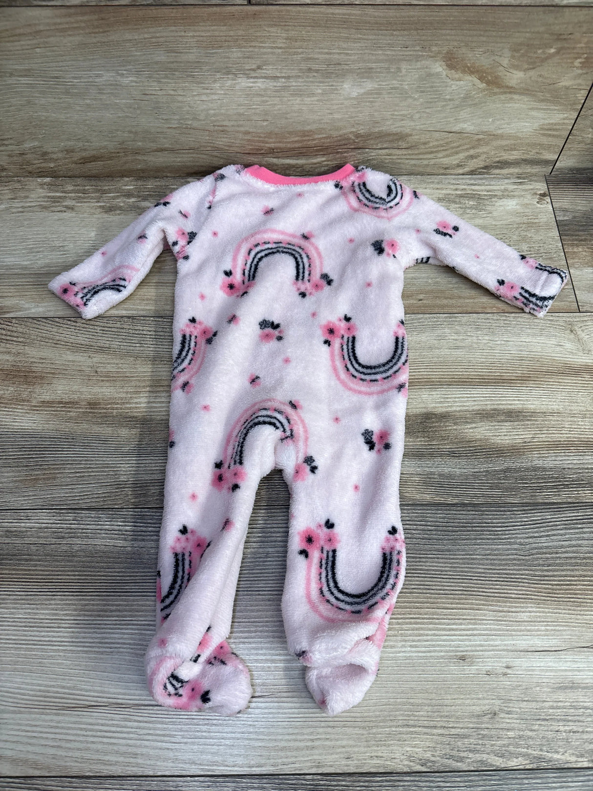 Pink fleece baby sleeper with rainbow and flower pattern, long sleeves, footed design on wood floor