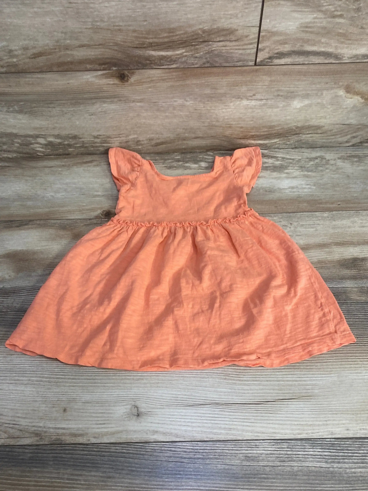 Flat lay of Cat & Jack toddler dress size 18M showcasing flutter sleeves and gathered waist in coral orange on wood floor