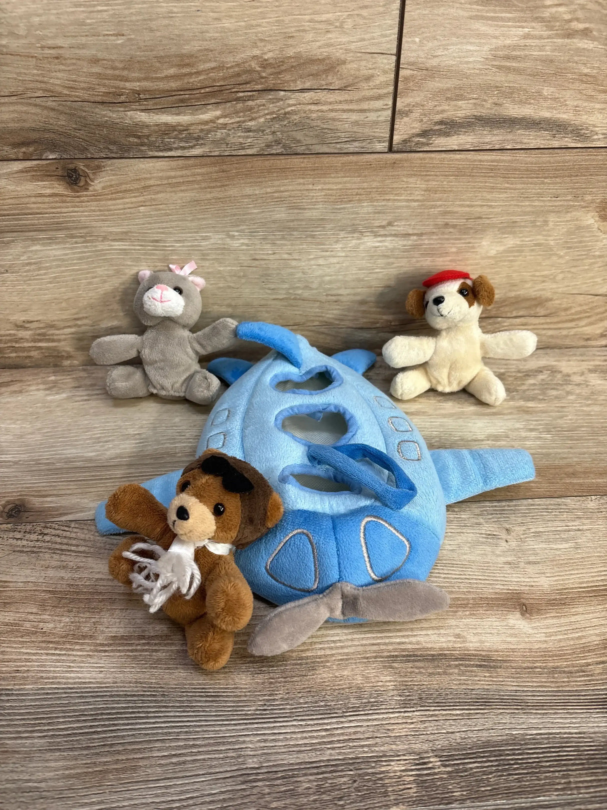 Angled top view of Unipak Designs blue plush airplane toy with three small animal finger puppets on wood background