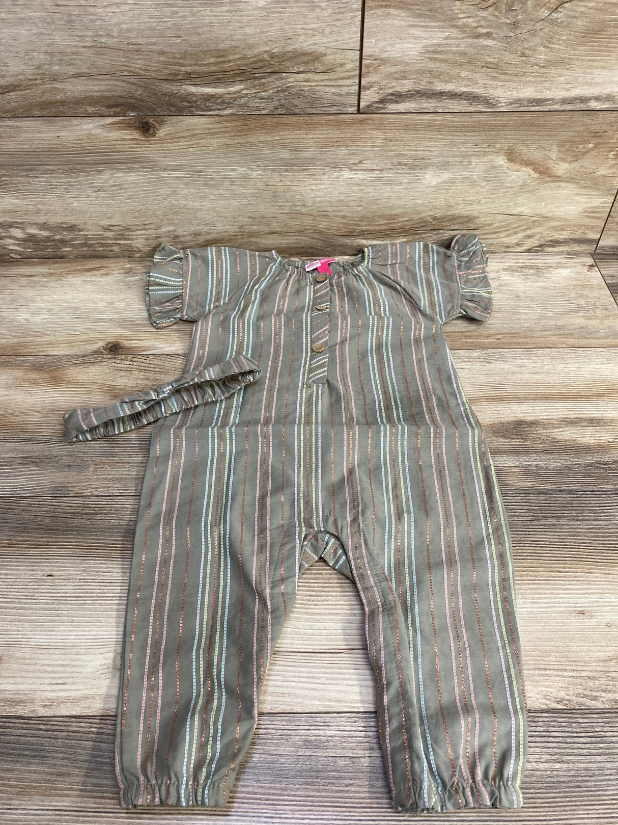 Flat-lay of Penelope Mack olive coverall with ruffle sleeves, button front, elastic ankles and matching headband on wood floor