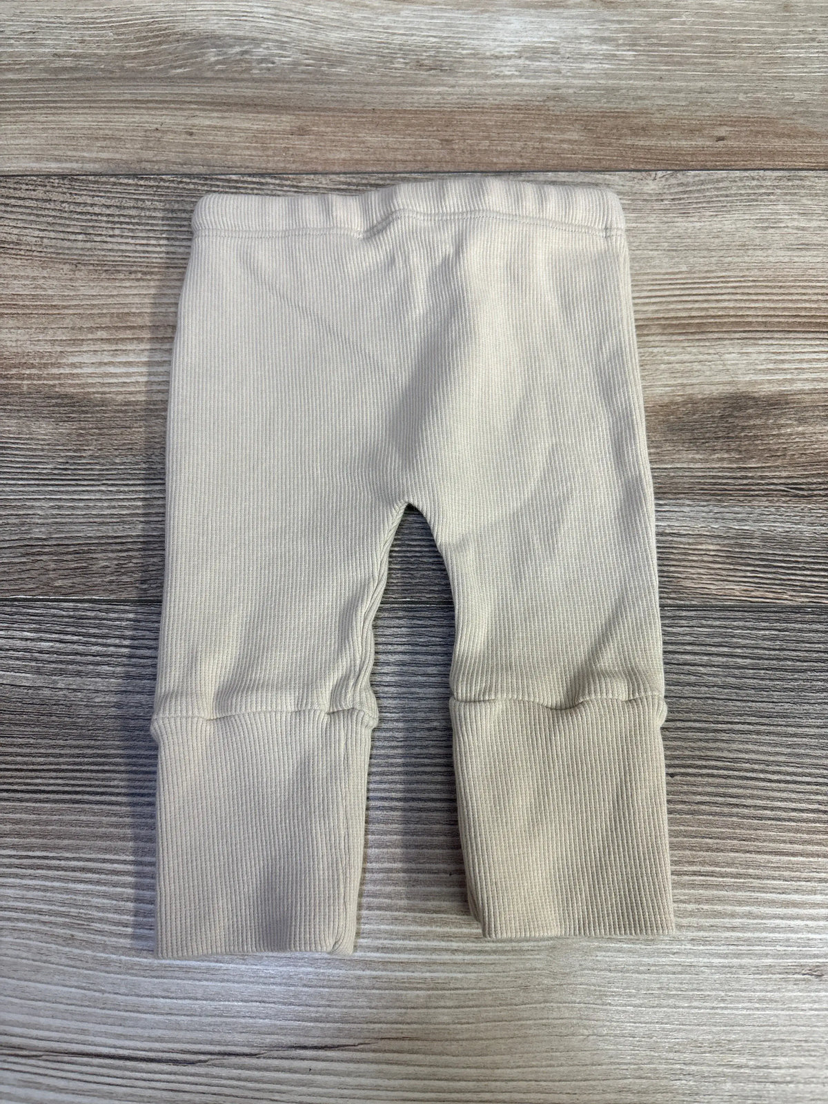 Front view of Grenalito newborn ribbed leggings in tan, with elastic waistband on a wood grain background
