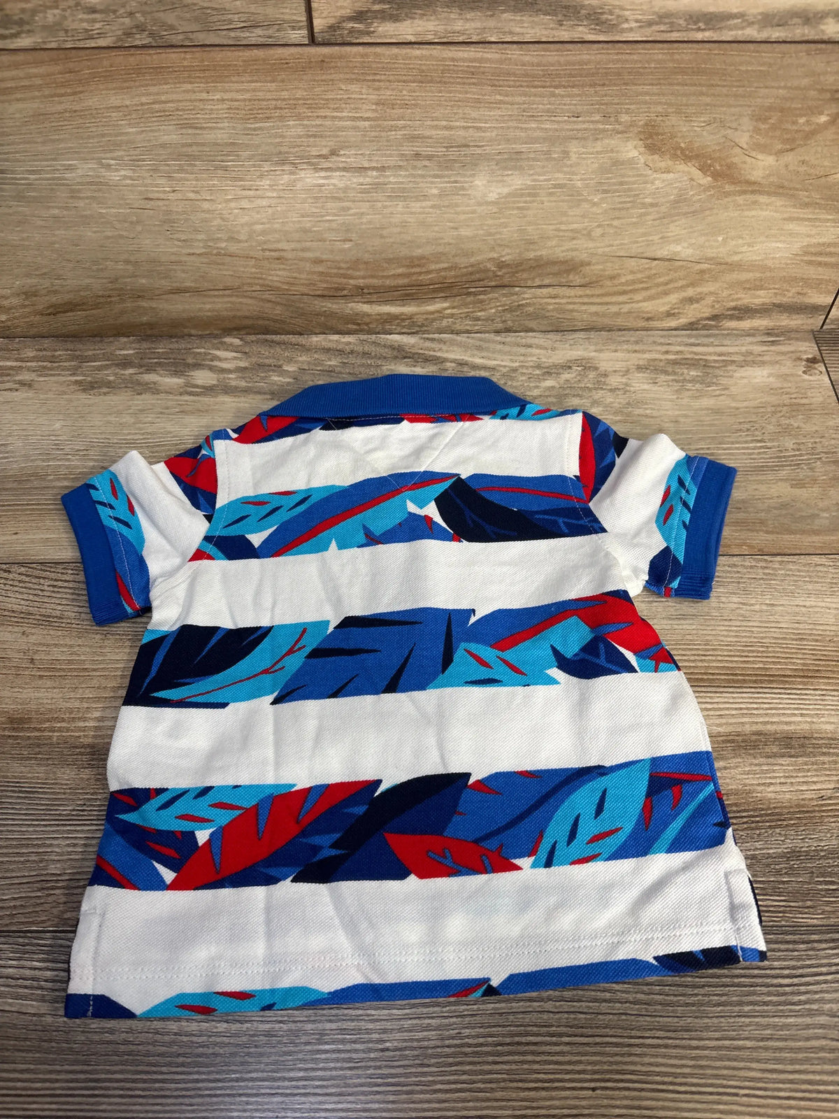 Front view of Tommy Hilfiger polo shirt showcasing white fabric with blue and red abstract pattern on a wood background