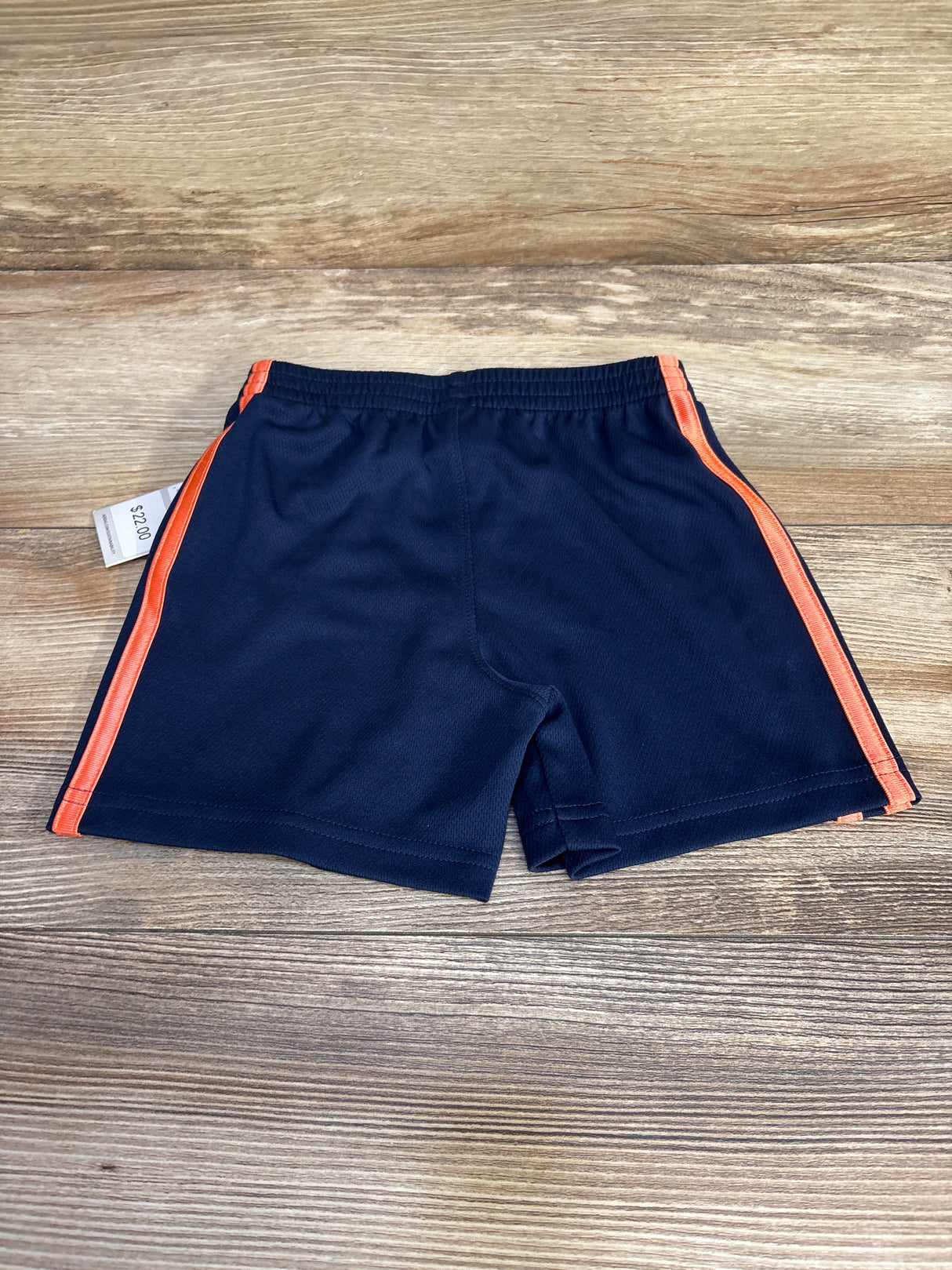 Navy blue athletic shorts with orange side stripes on wood background, $2.00 price tag