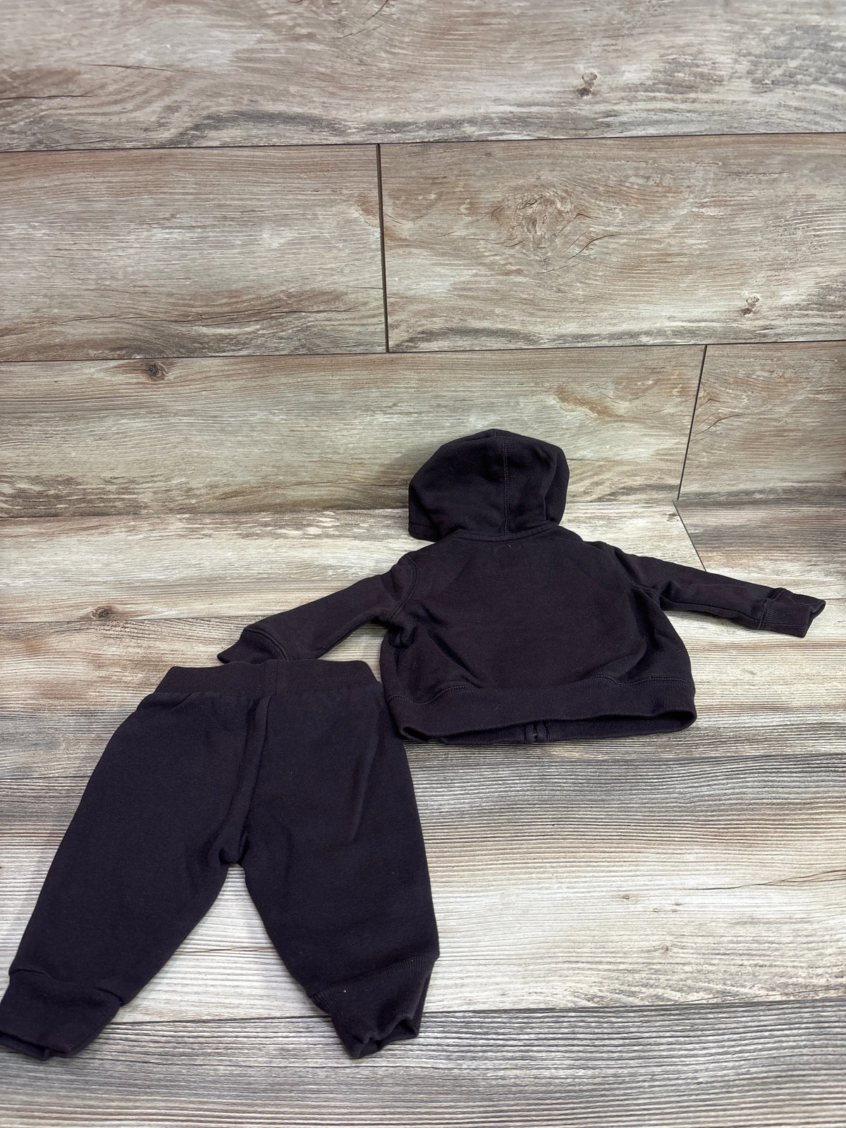 Back view of Baby Gap two-piece zip-up hoodie and joggers set in black with a hood and cuffed hems on a wood-look background