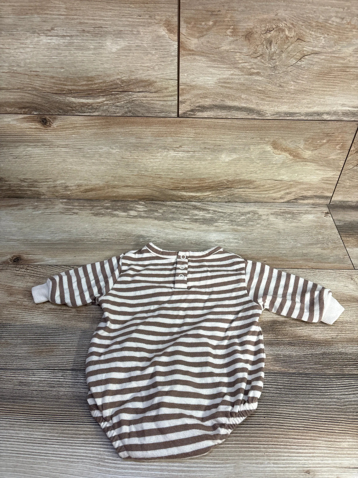 Front view of Easy Peasy striped sweatshirt bubble romper in beige with long sleeves and snap placket on a wood-look background