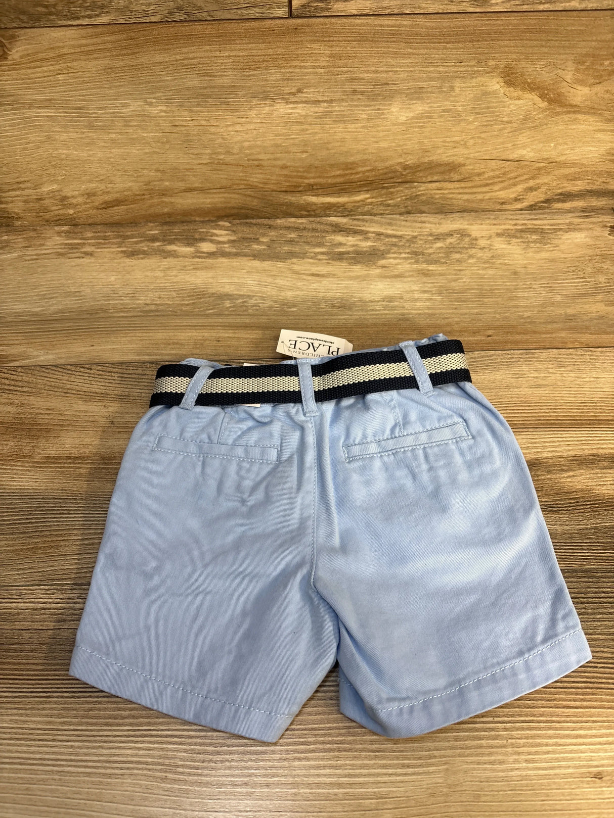 Back view of light blue belted chino shorts size 12-18M showing striped elastic belt and back welt pockets on wood