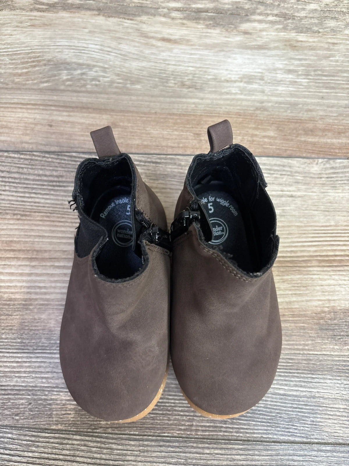Pair of brown toddler leather boots with side zipper and pull tab on wooden floor