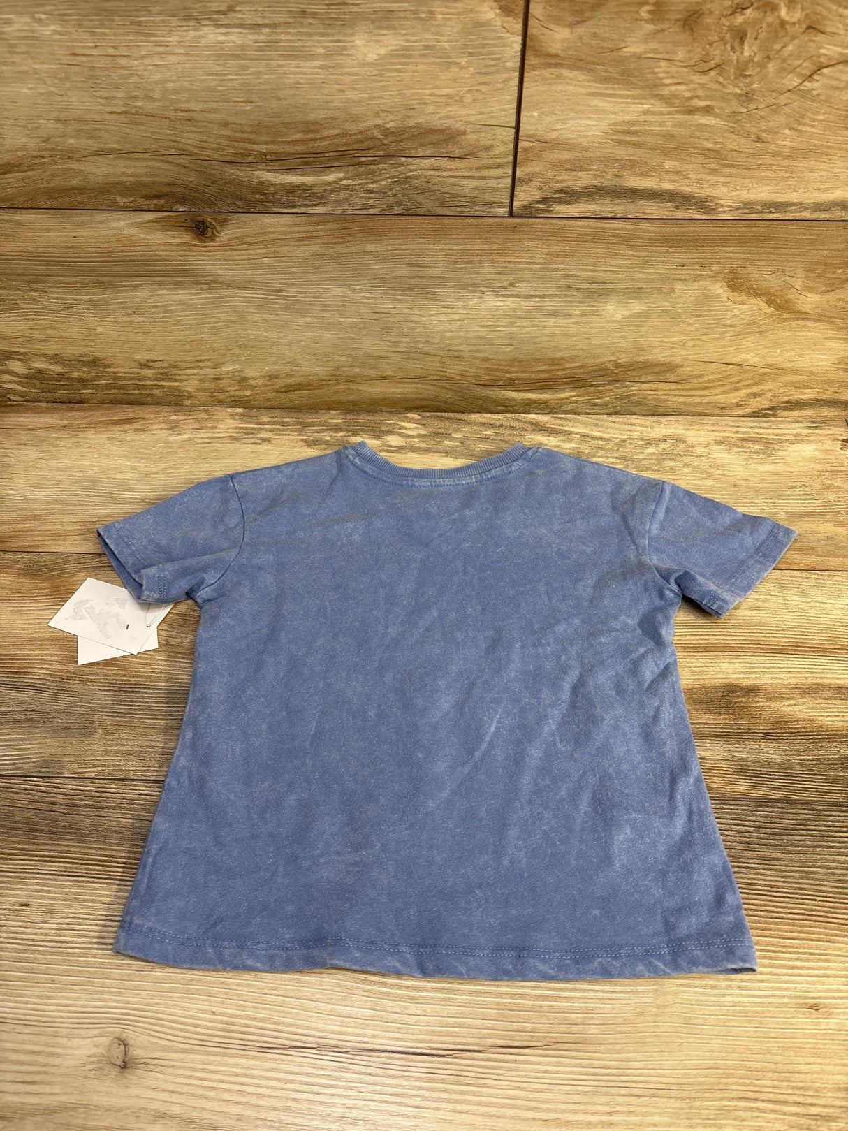 Flat-lay back view of Grayson Mini short-sleeve toddler shirt in washed blue showing crew neck and tags on wood background