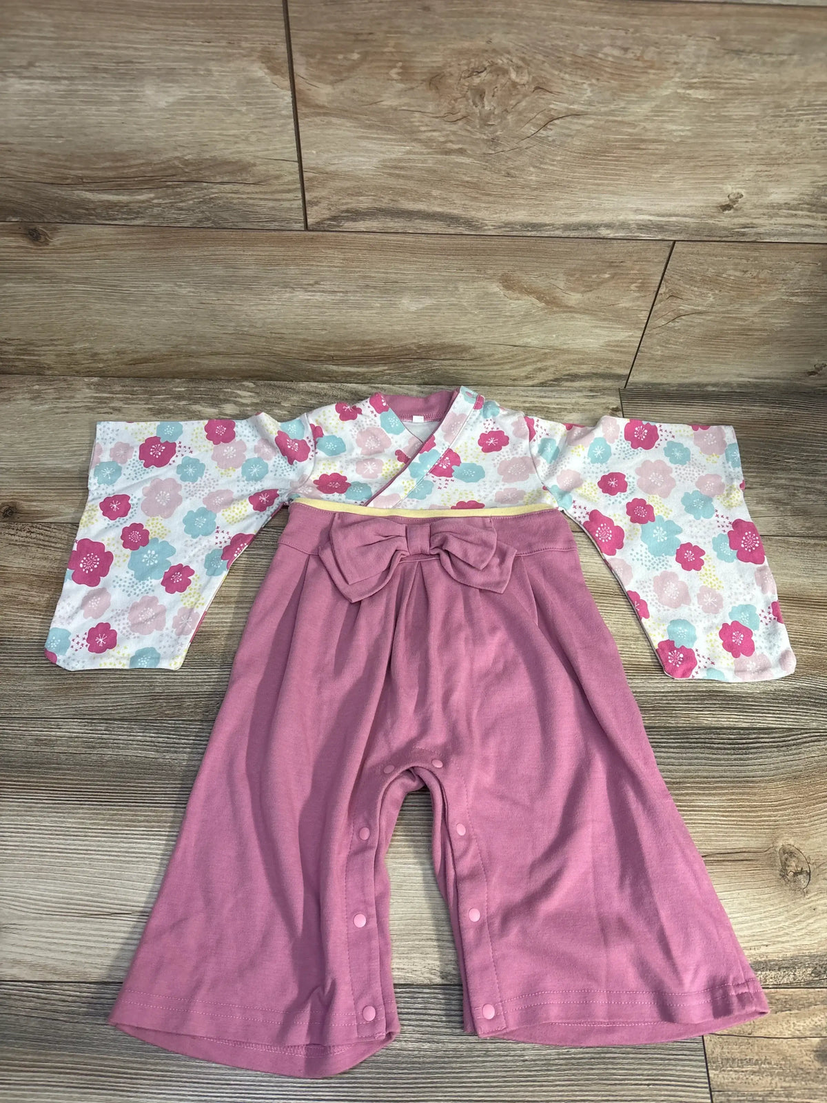 Baby kimono romper with floral top and pink bow pants on wood background