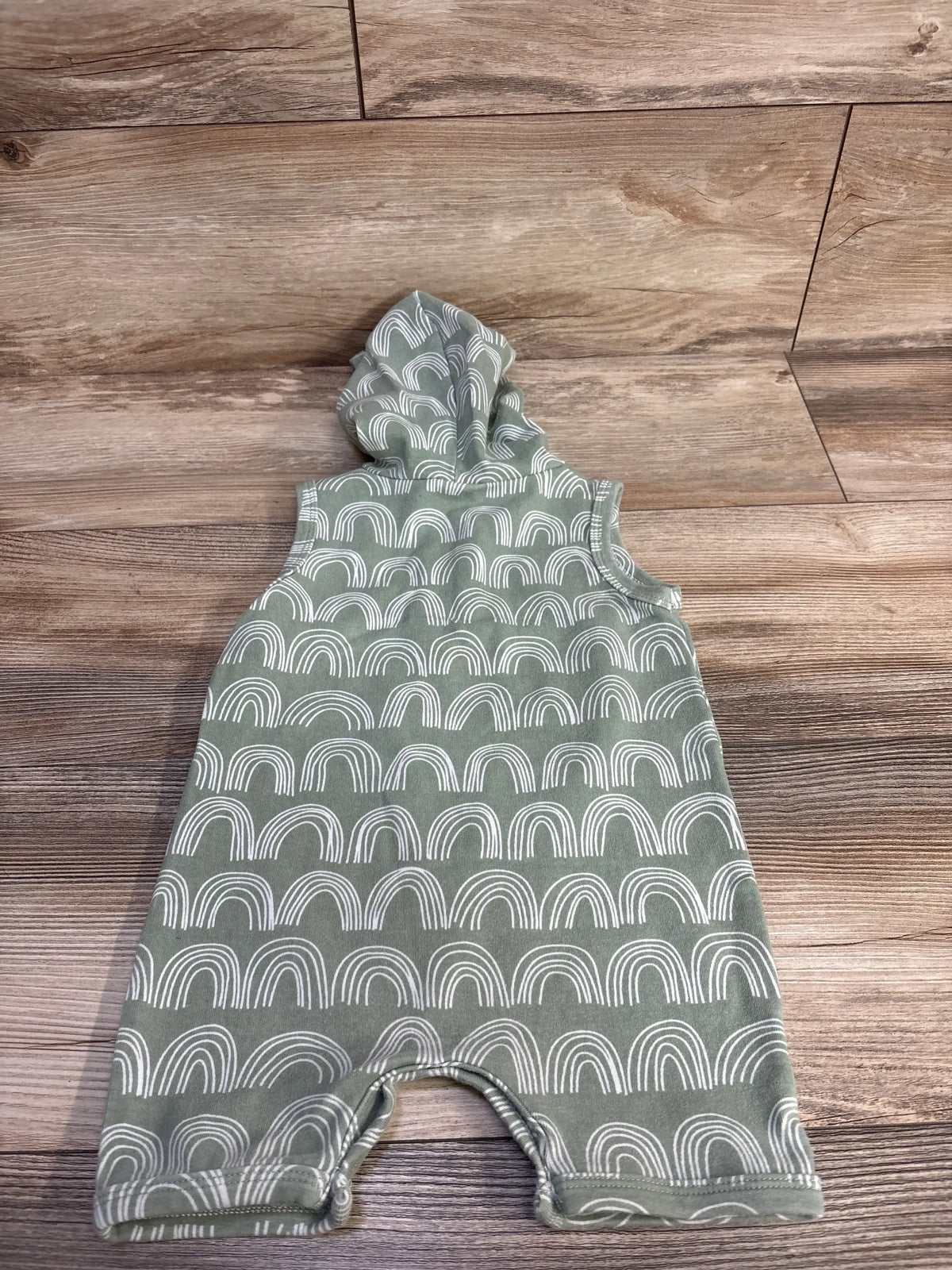 Front view of Little One Shop green hooded Henley shortie romper with white rainbow pattern on a wood floor