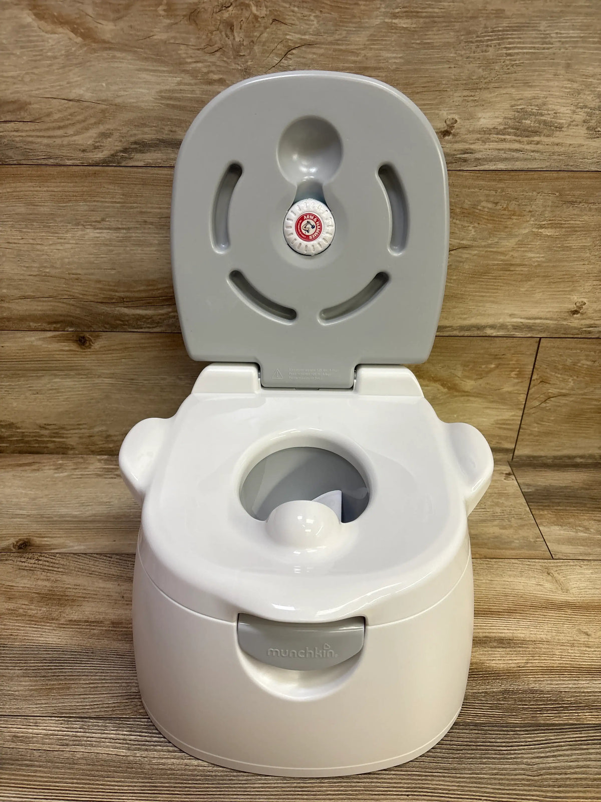 Front view of Munchkin Arm and Hammer Multi Stage 3 in 1 Potty showing open lid and round insert on a wood floor