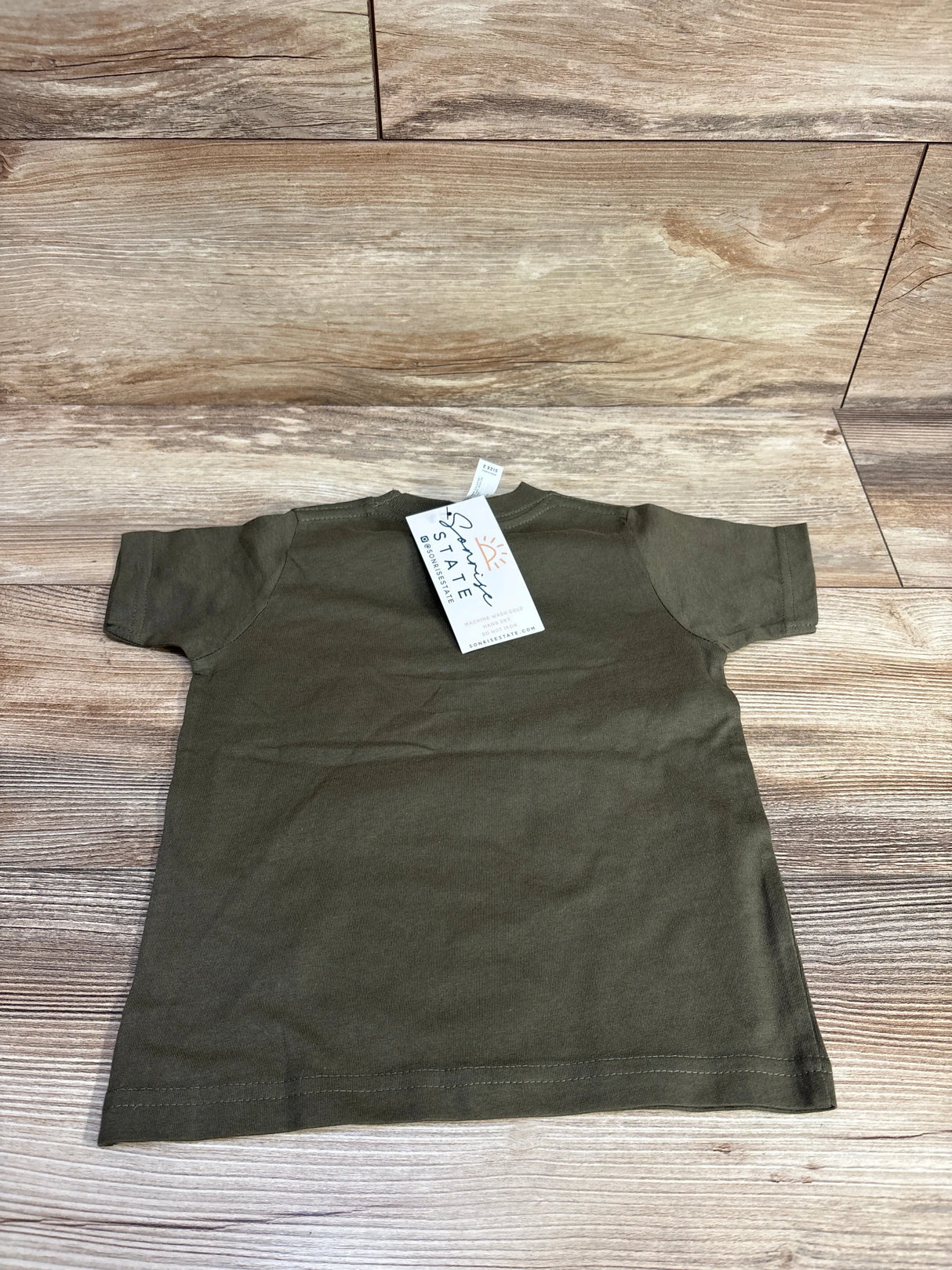 Olive green short sleeve toddler t-shirt with tag on wood background