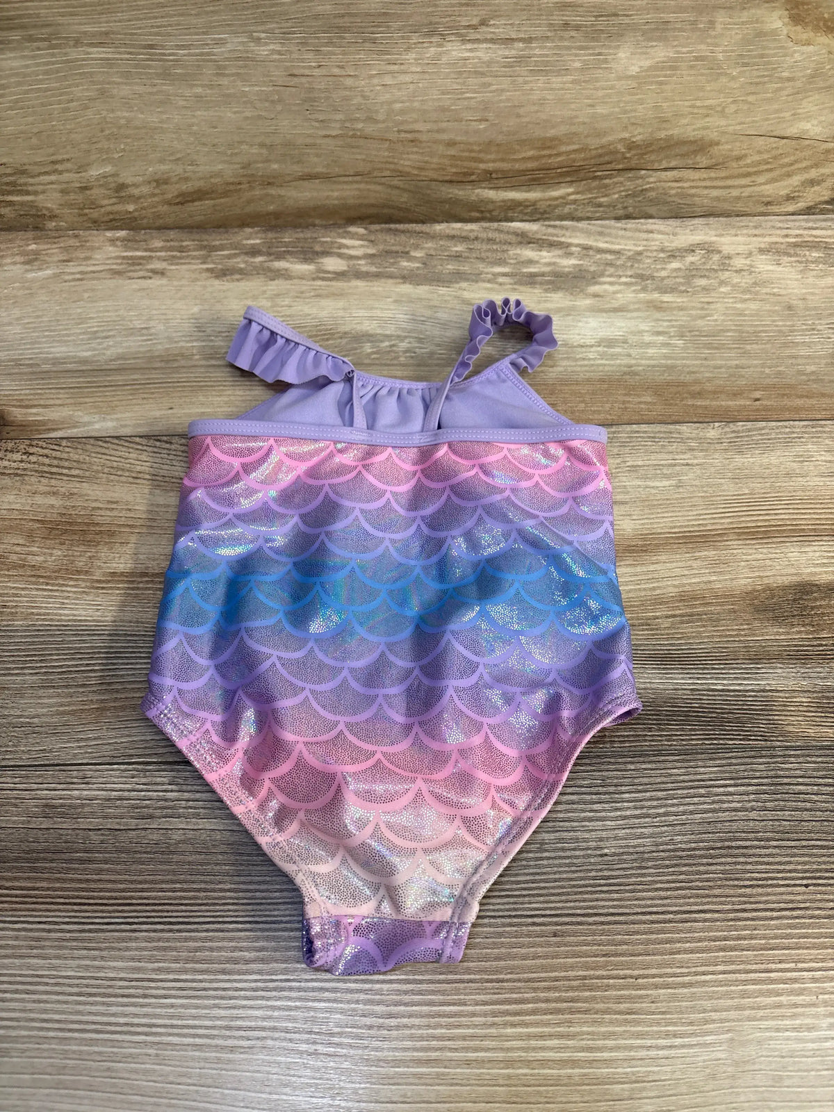 Flat lay of Sol Borne purple one-piece mermaid swimsuit showcasing ruffled straps and iridescent scale pattern