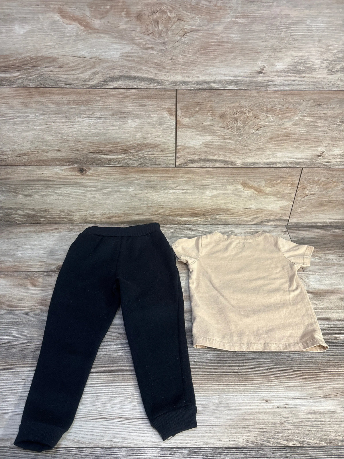 Top-down view of toddler 2-piece jogger set with beige short-sleeve tee and black cuffed pants on wood flooring
