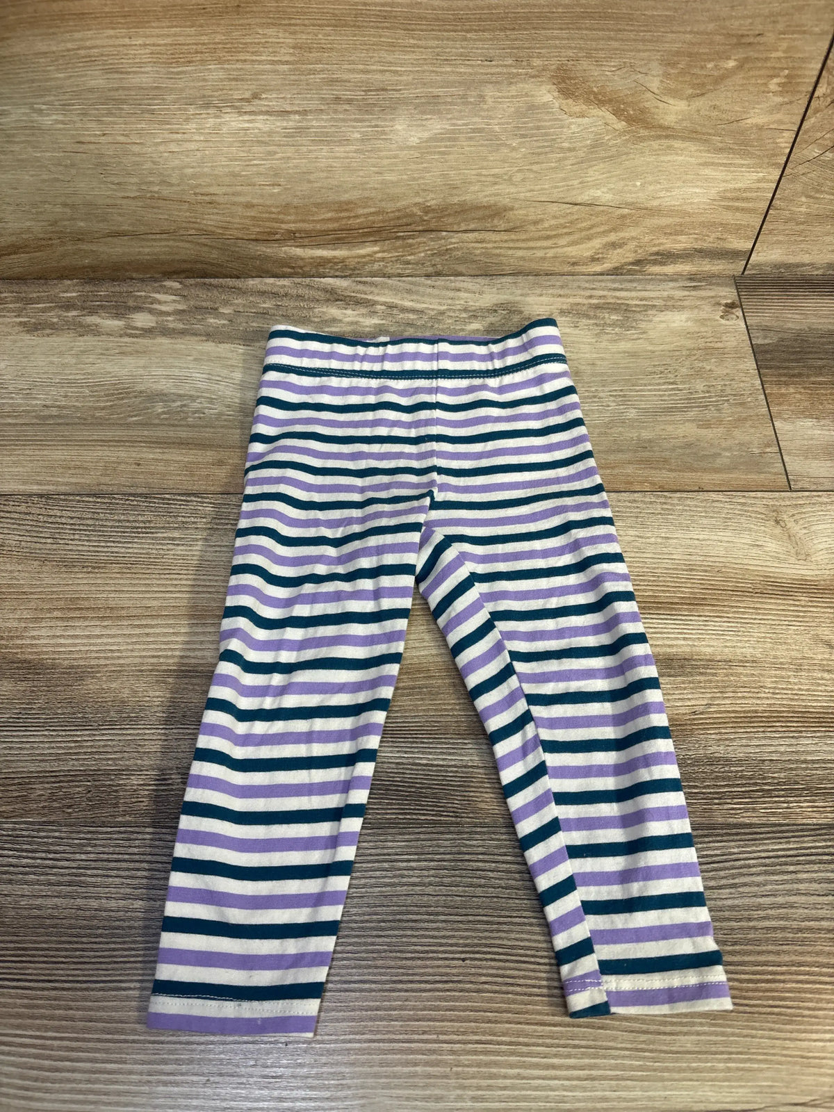 Front view of Dip striped leggings in white with purple and dark teal horizontal stripes, laid flat on a wood floor
