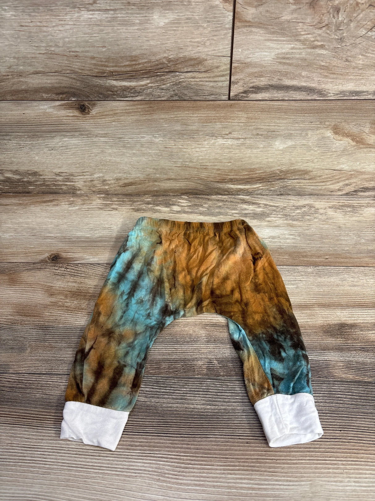Tie-dye baby pants with blue and brown colors, white ankle cuffs, on wood background