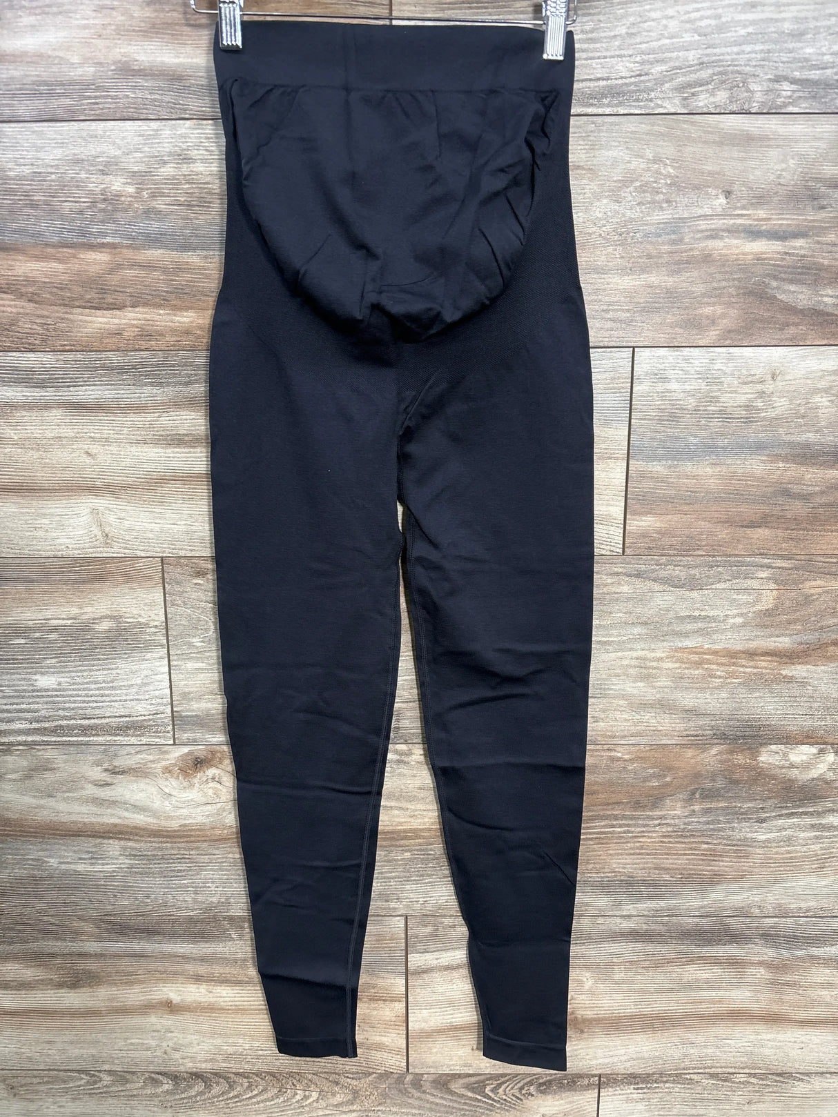 Black high-waisted maternity leggings on hanger, shown on wooden background