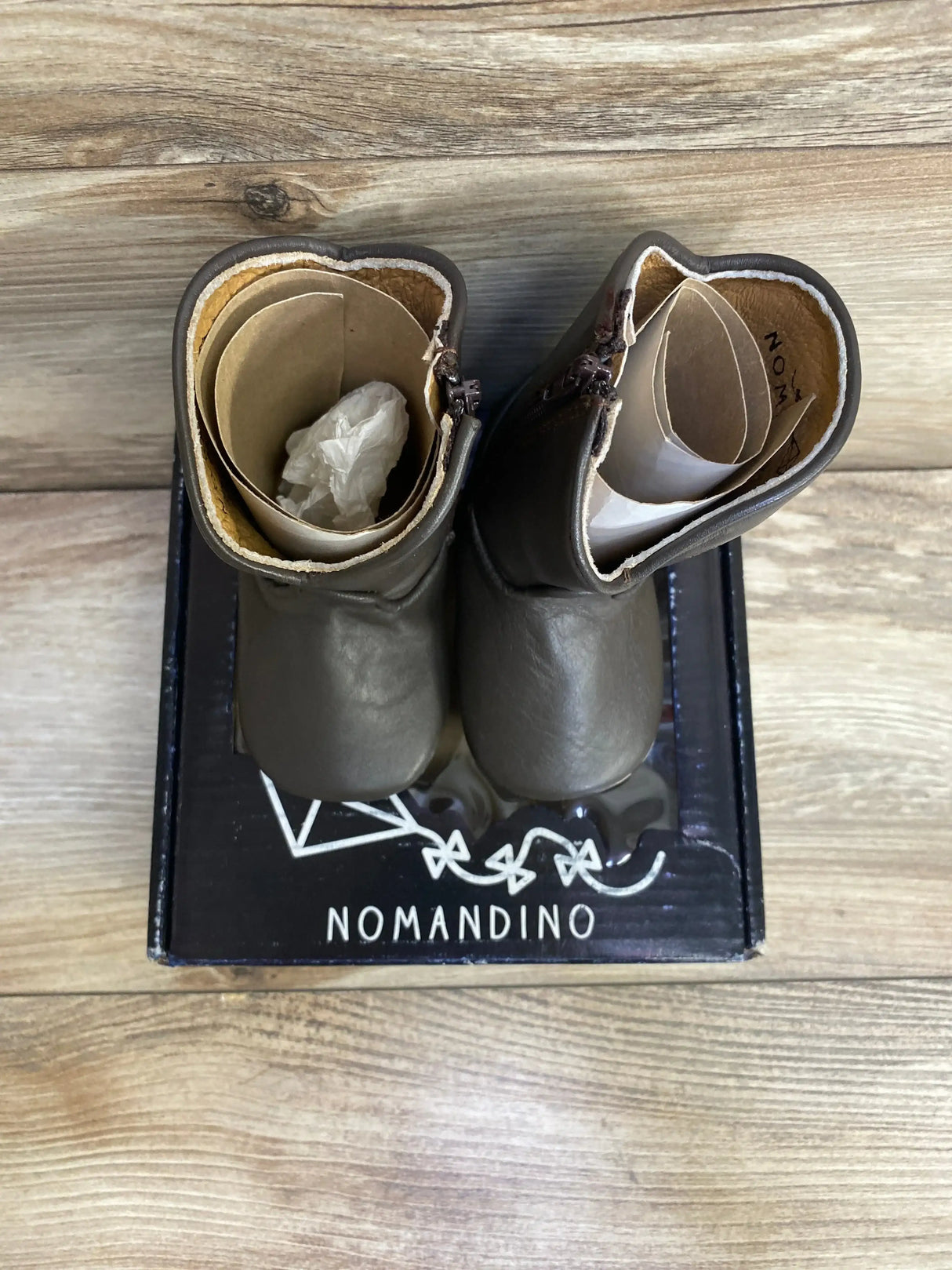 Top view of Nomandino Spark chocolate brown leather baby boots displayed on branded box with wood plank background