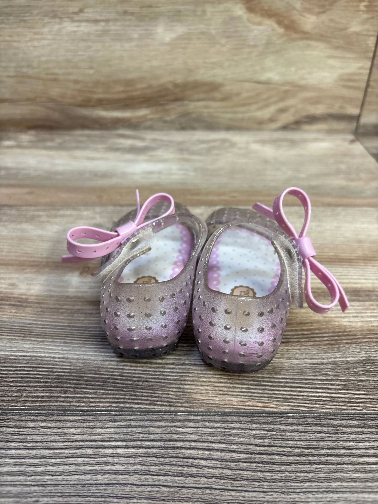 Front view of Mini Melissa Ultragirl jelly Mary Jane shoes with silver glitter, pink bows and perforated toe on wood