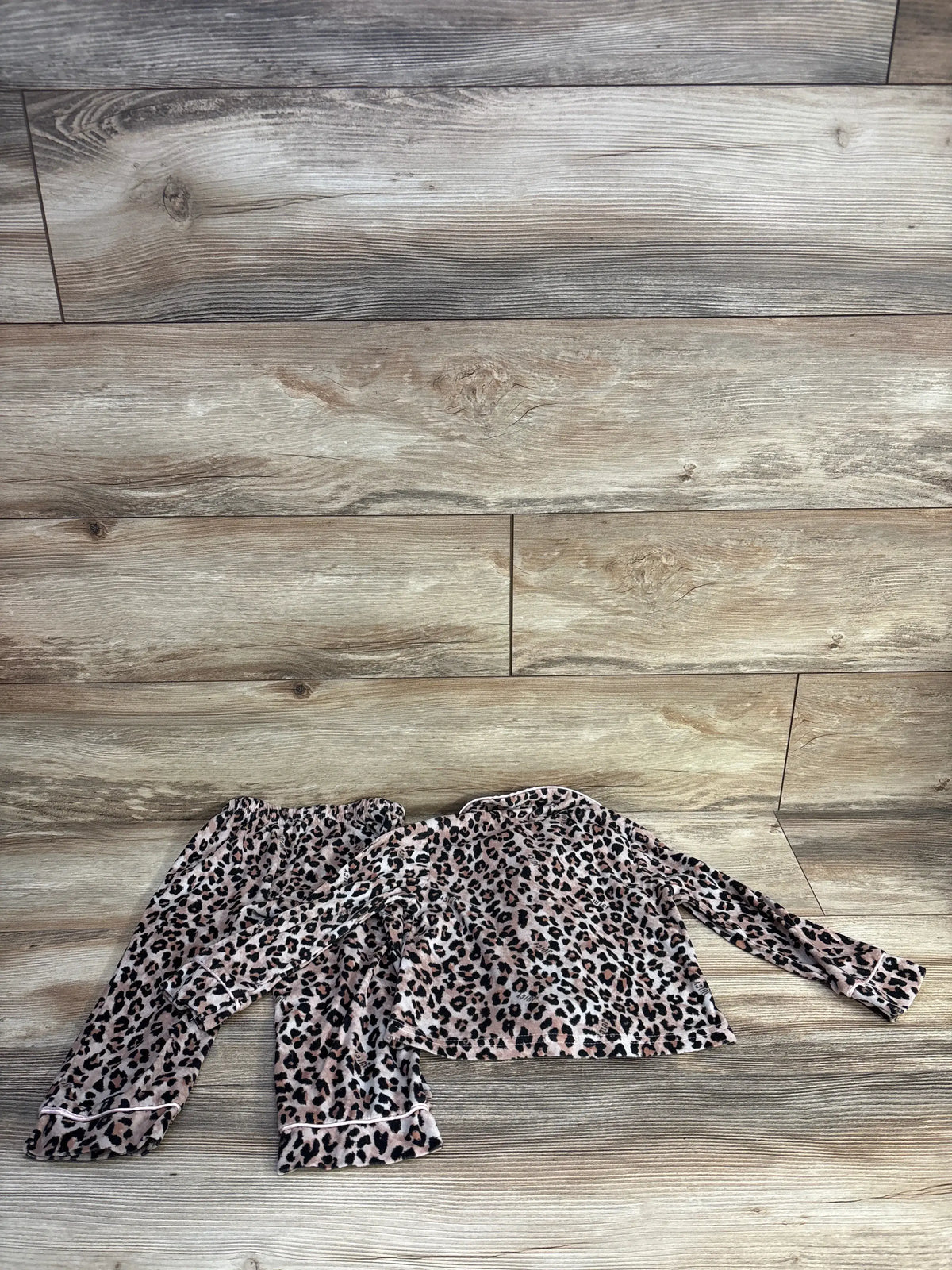 Flat lay of Juicy Couture leopard coat-style pajama set showing beige leopard print top and matching pants on wood floor