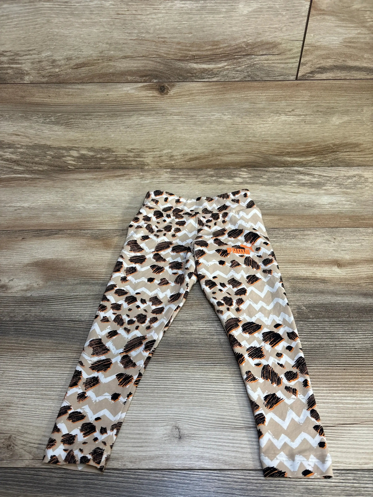 Kids leopard print leggings with chevron pattern, Puma logo, laid on wood floor