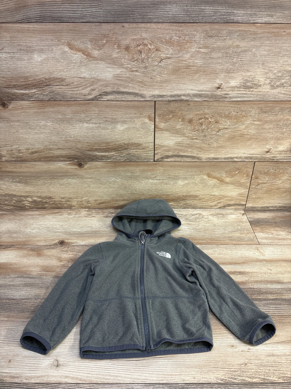 Front view of The North Face Glacier fleece hoodie for toddler showcasing full zipper, hood, and fleece texture with wood background