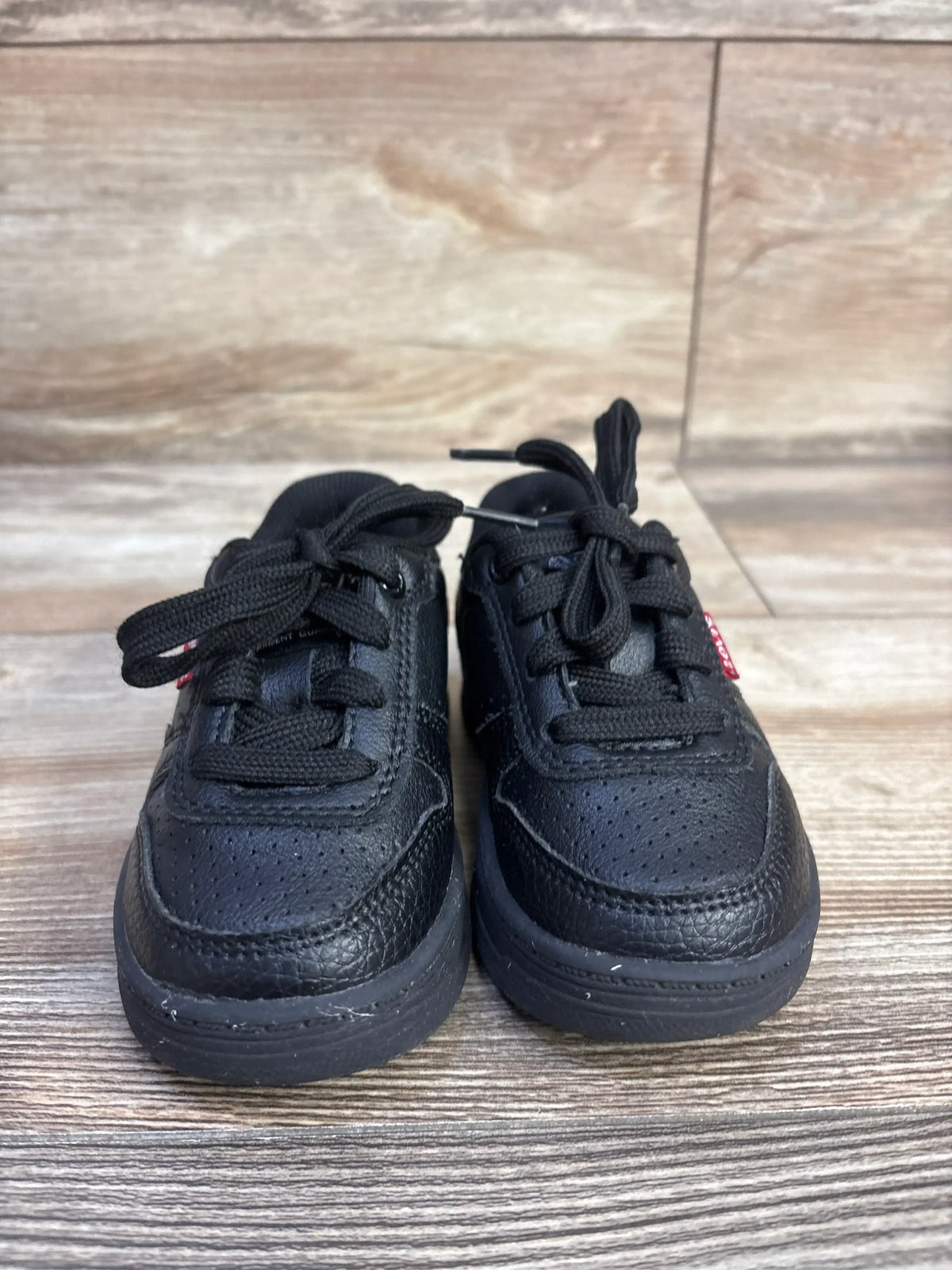 Front view of black Levi’s Drive Lo Sneakers, size 6C, with perforated toes and rubber outsoles on wood-look flooring