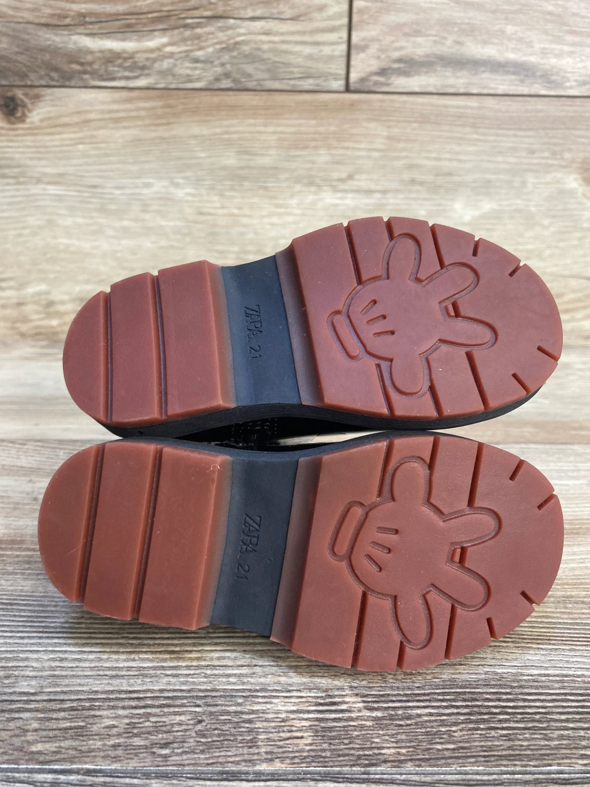 Children's shoes with red soles and cartoon glove imprint, size 21, on wood floor