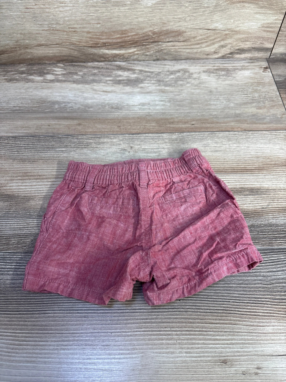 Flat lay of newborn red baby shorts showcasing elastic waistband, back pockets, and rolled hems on wood background
