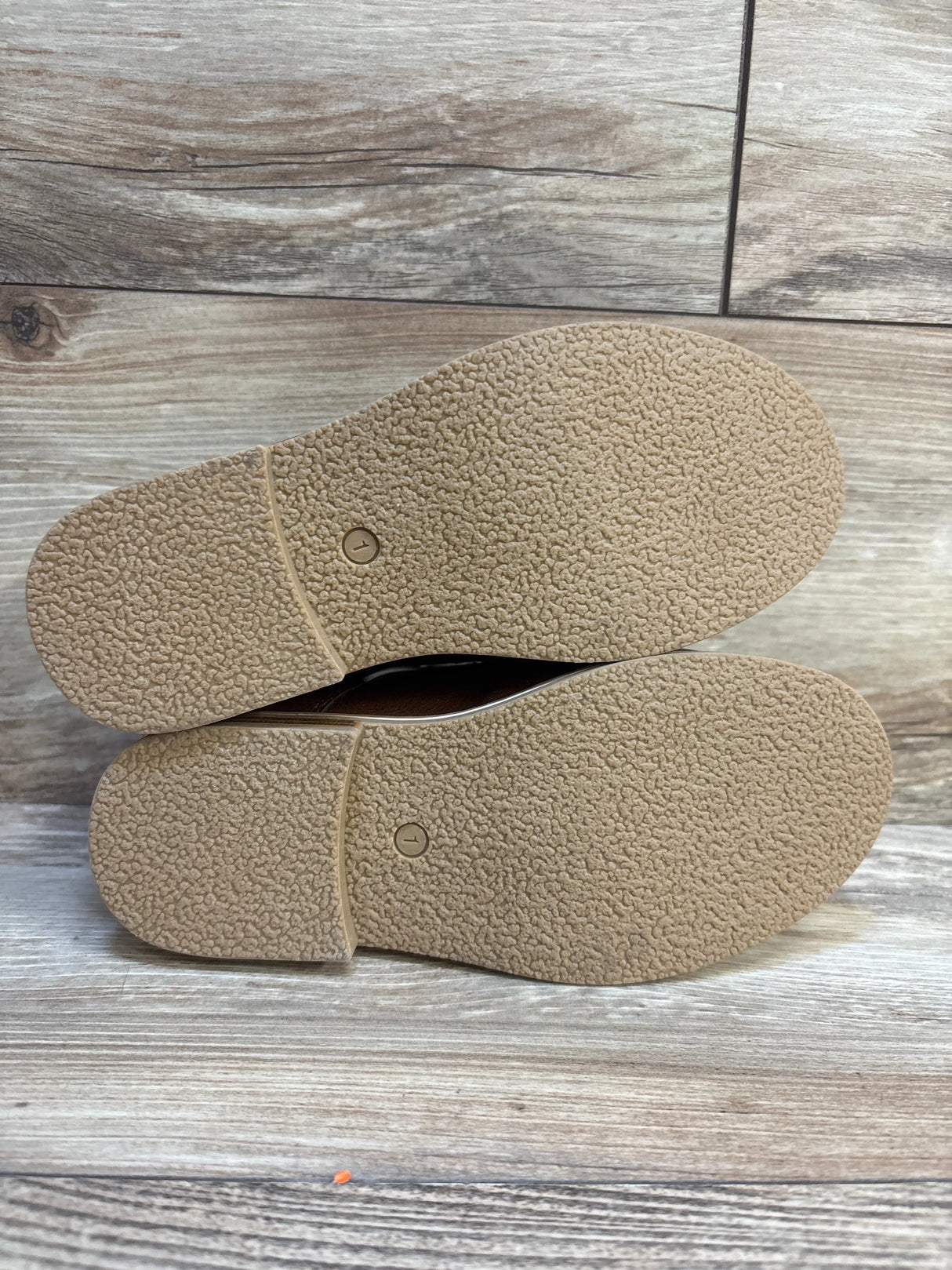 Sole view of pair of kids shoes showing tan textured rubber outsoles on wood plank floor