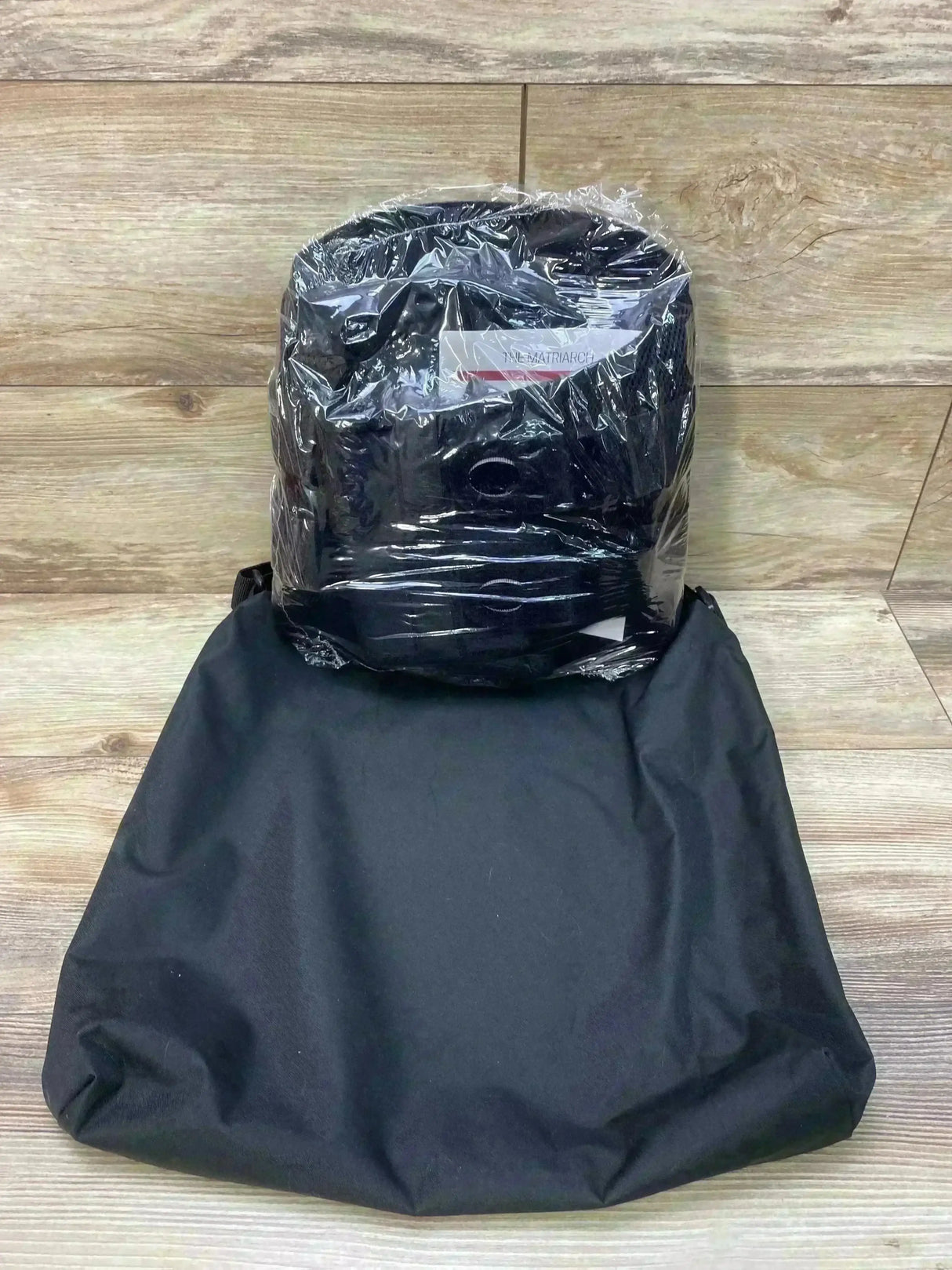 Front view of Matriarch pregnancy support belt in clear plastic with adjustable straps and black storage bag on wood floor