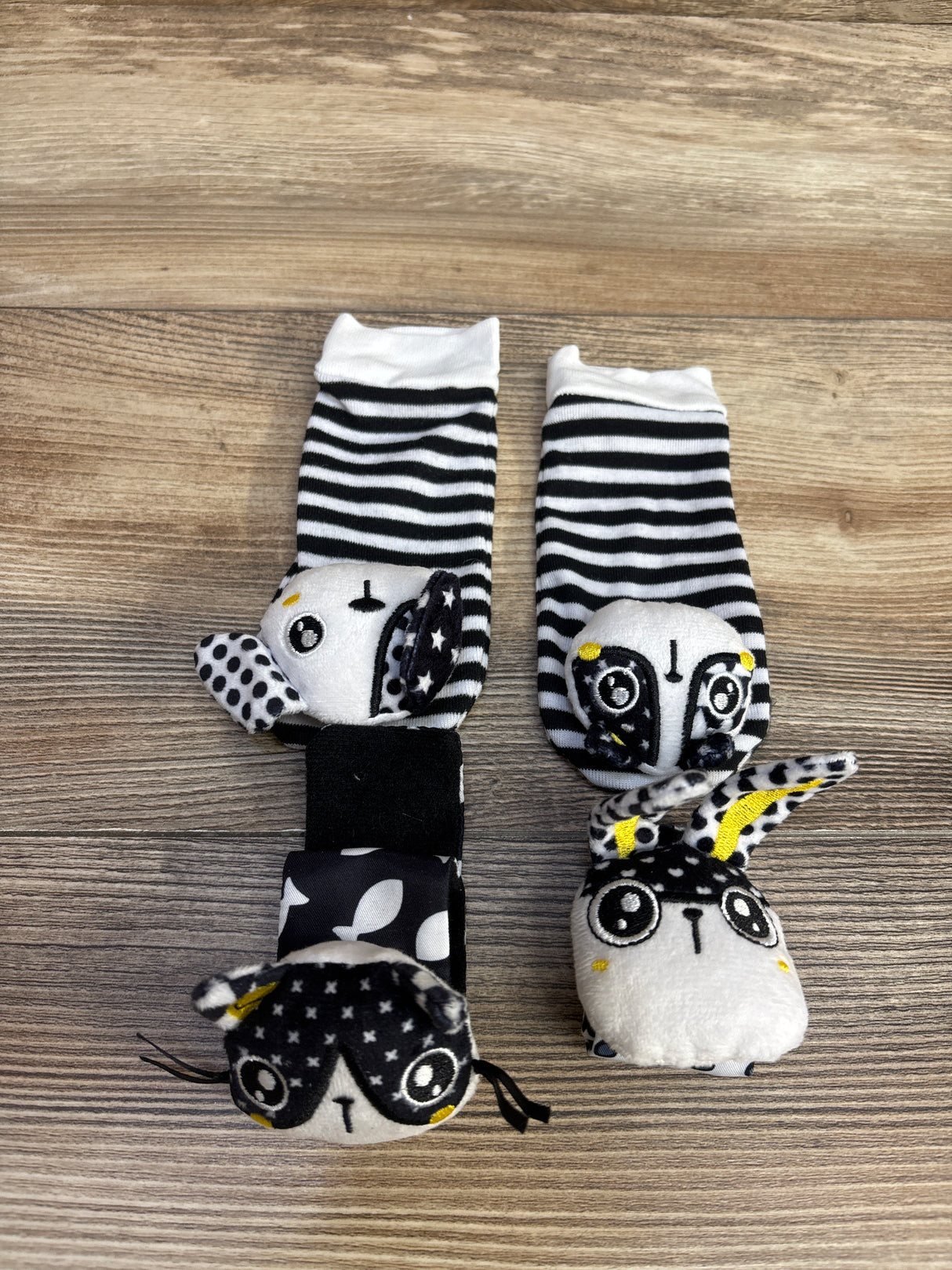 Black and white striped baby socks and wrist rattles with animal faces on wood floor