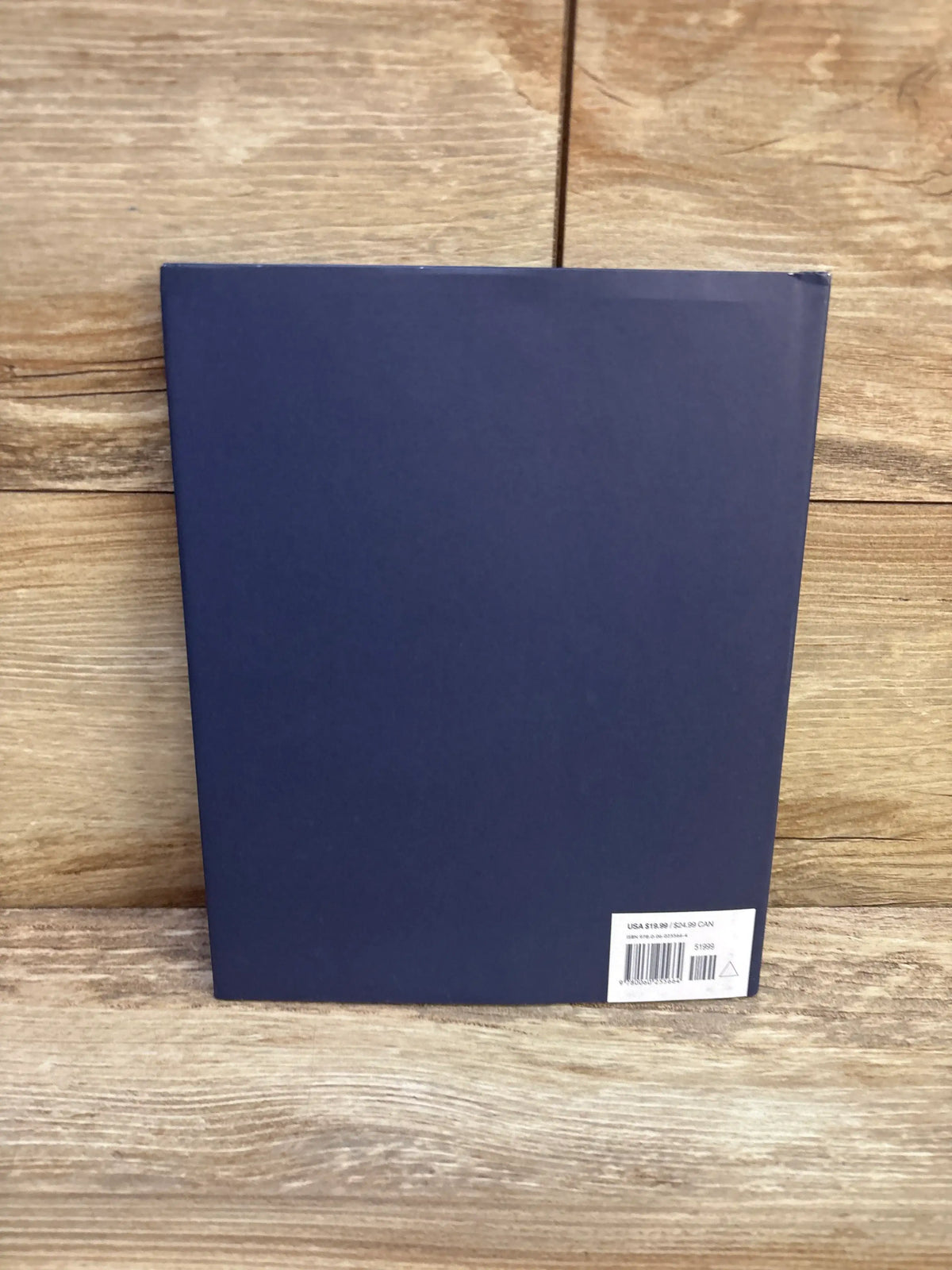 Back of It Looked Like Spilt Milk hardcover showing navy back cover with barcode sticker on lower-right on wooden surface