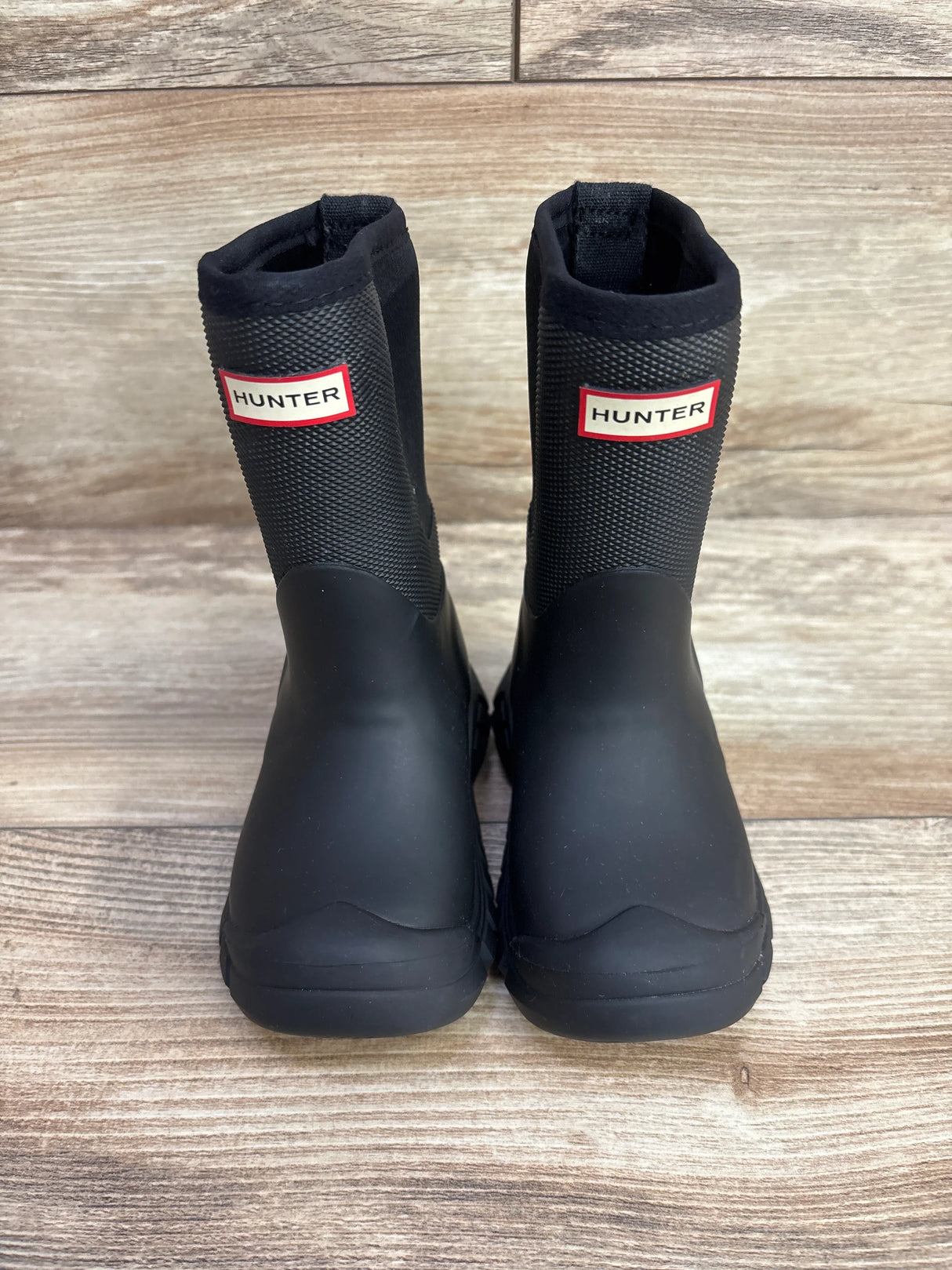Pair of black Hunter brand rain boots for children on wooden floor background