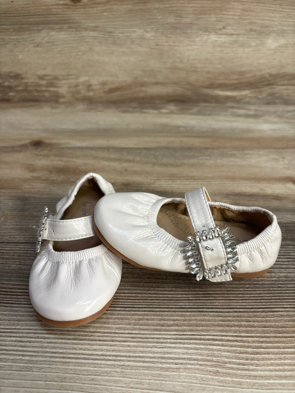 White baby girl shoes with jewel buckles on wooden surface