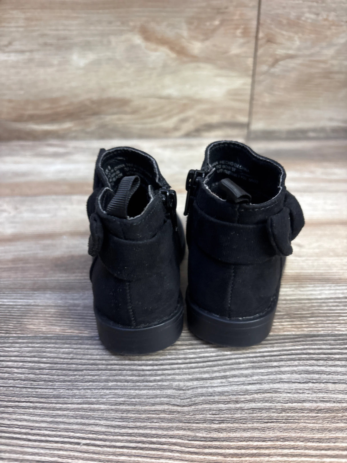 Rear view of Baby Gap black bow ankle boots showing back zipper and bow detail on wood-grain surface