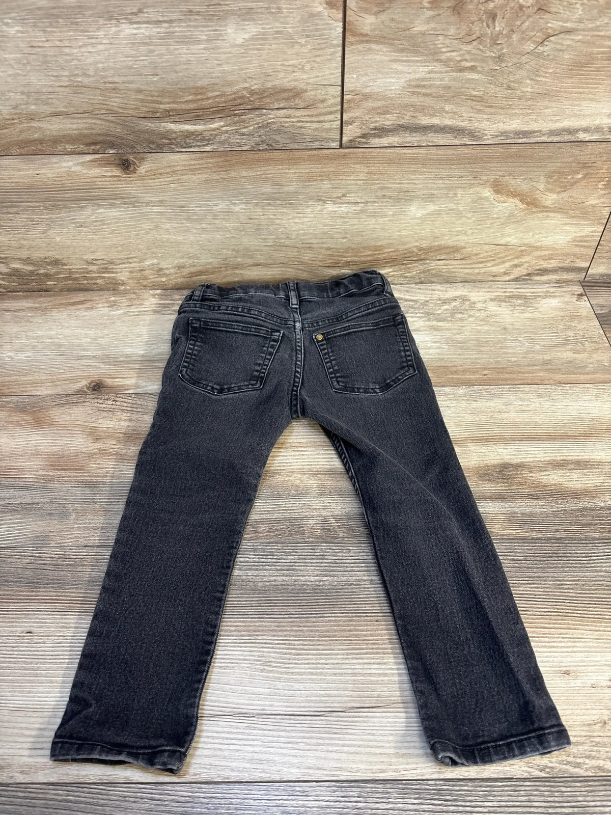 Black denim kids jeans with back pockets laid flat on wood floor