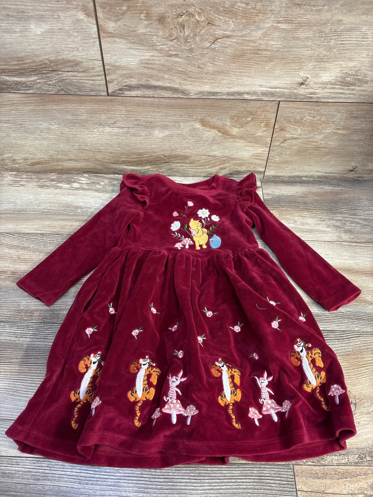 Flat lay of Disney maroon long-sleeve toddler dress 3T with embroidered Pooh Tigger Piglet and floral details on wood floor