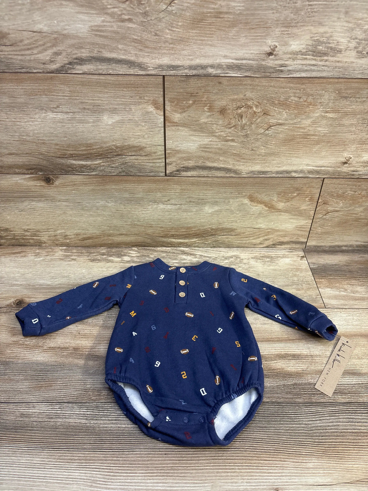 Flat lay of Nicole Miller navy football print bubble romper with henley buttons size 6-9M on wood background