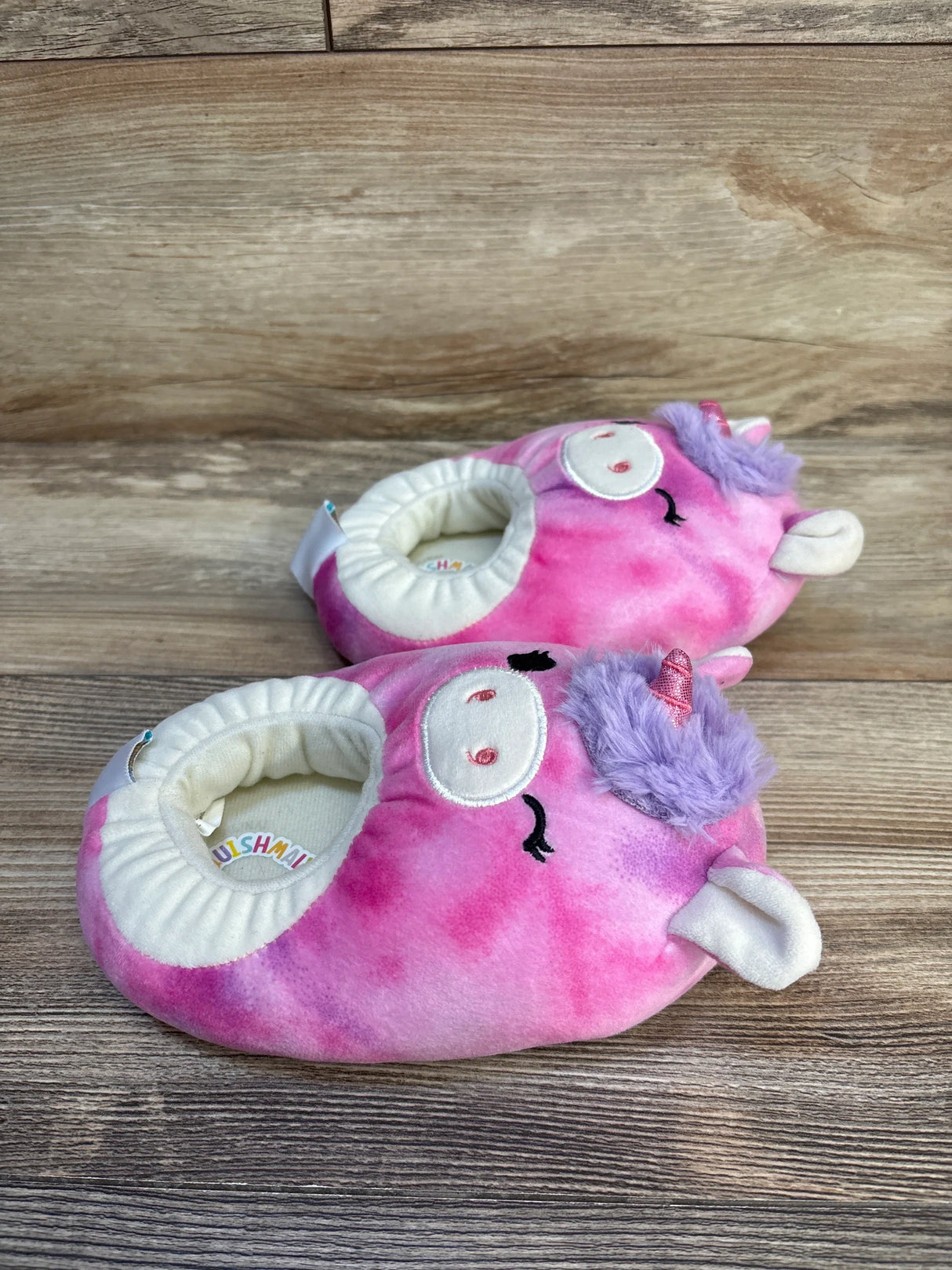 Pink unicorn plush baby slippers with purple mane and horn on wooden floor