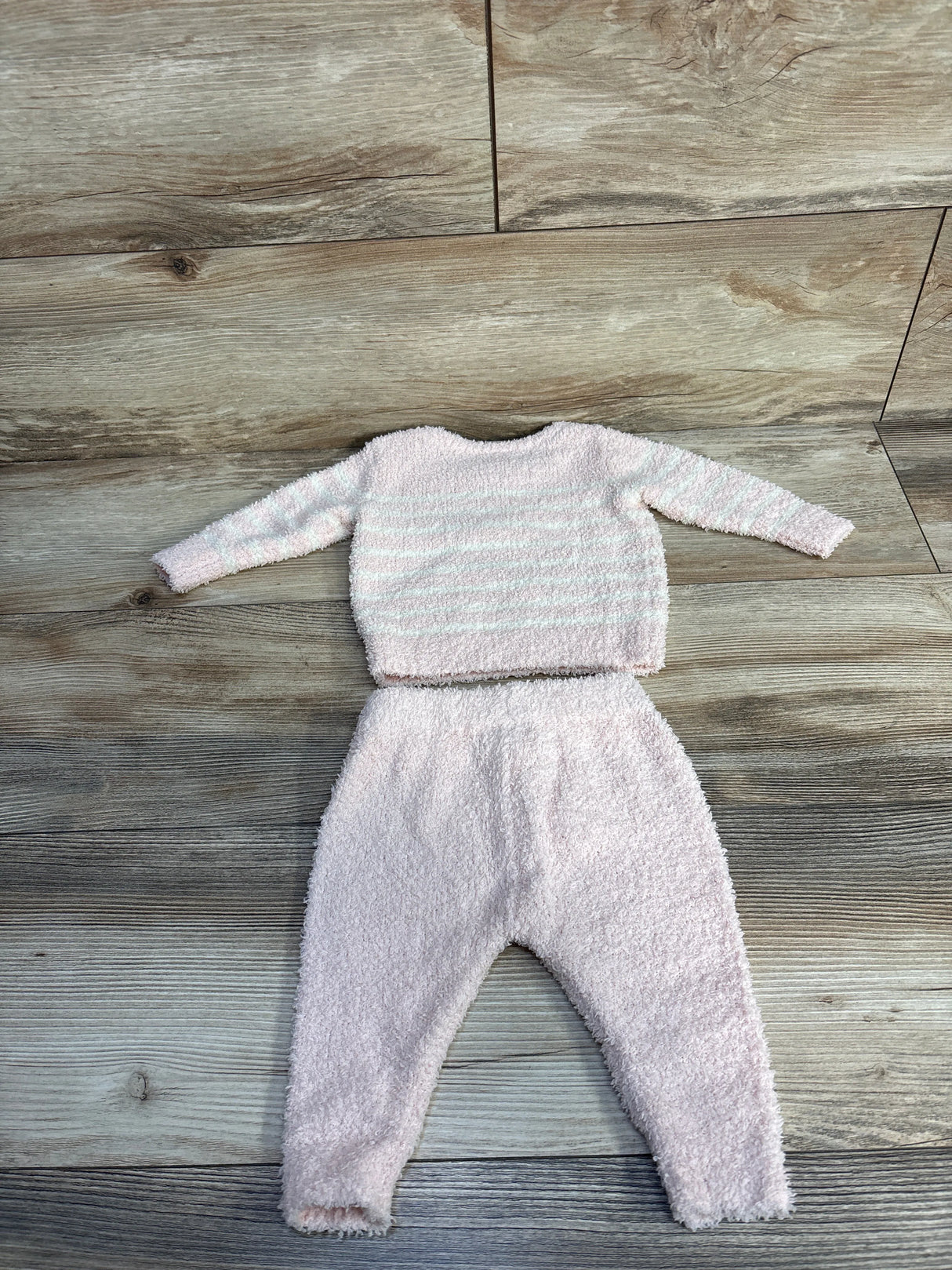 Soft pink striped baby sweater and pants set on wooden floor