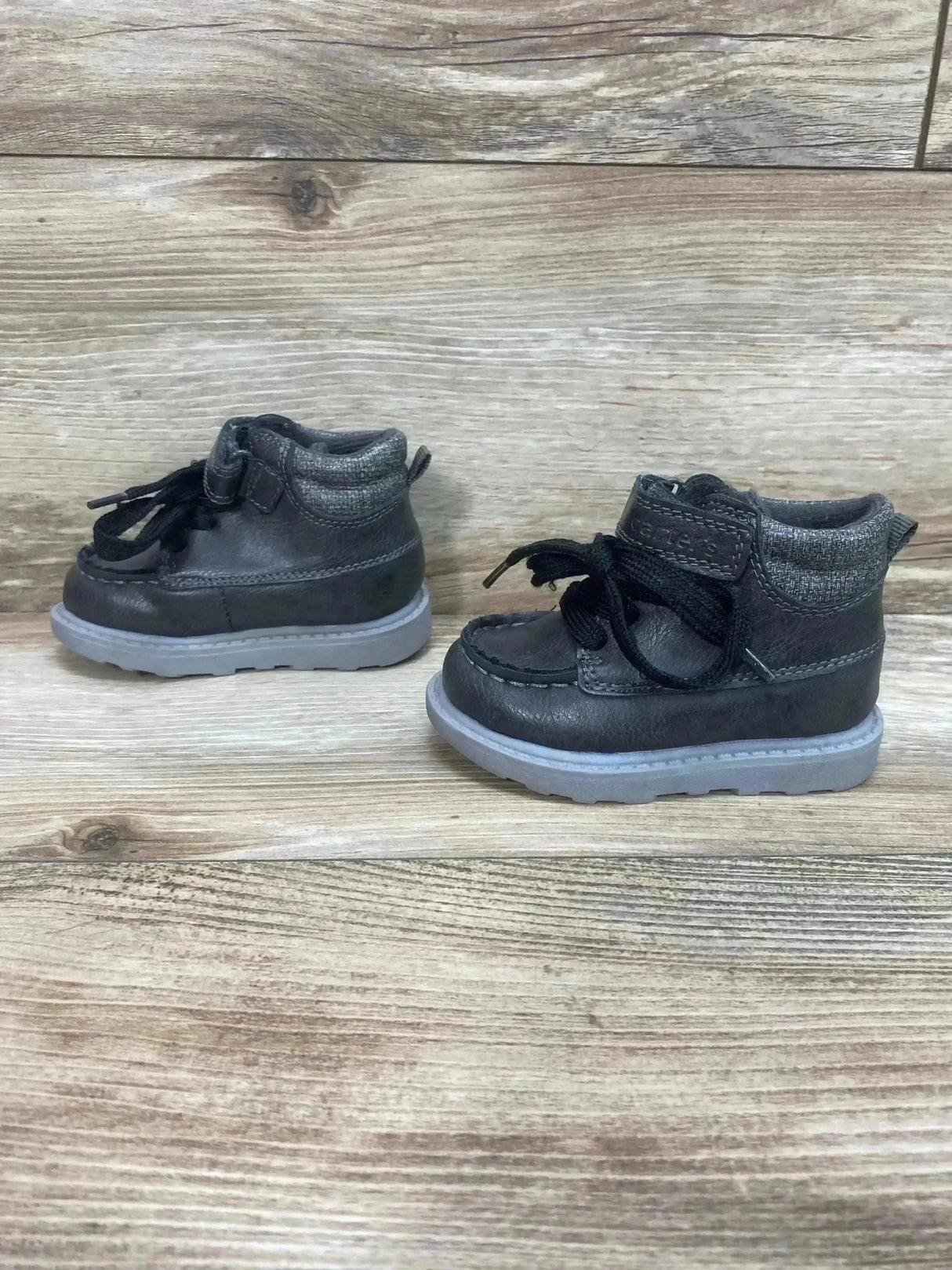 Side view of Carter’s Norman boys grey ankle boots with laces and Velcro strap, padded knit collar, and light grey sole on wood background
