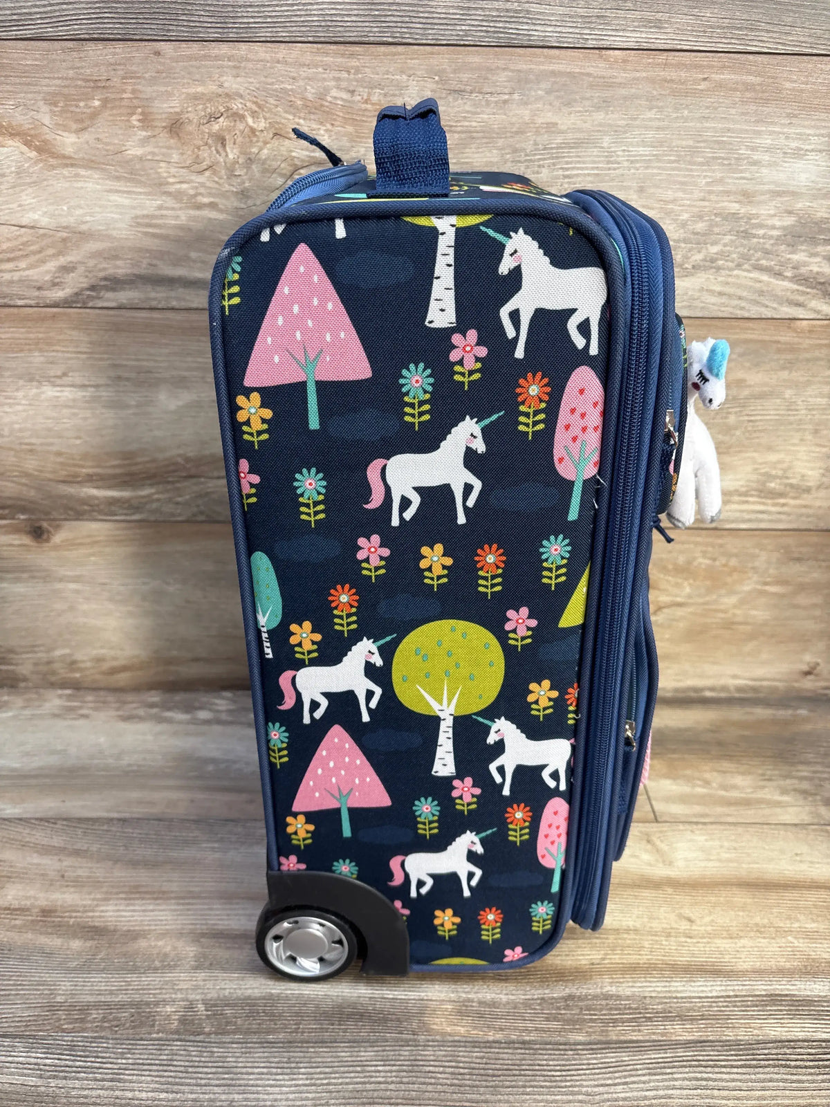 Front view of Crckt Kids Softside Carry On Suitcase in unicorn design showcasing side zippered pocket on wood floor