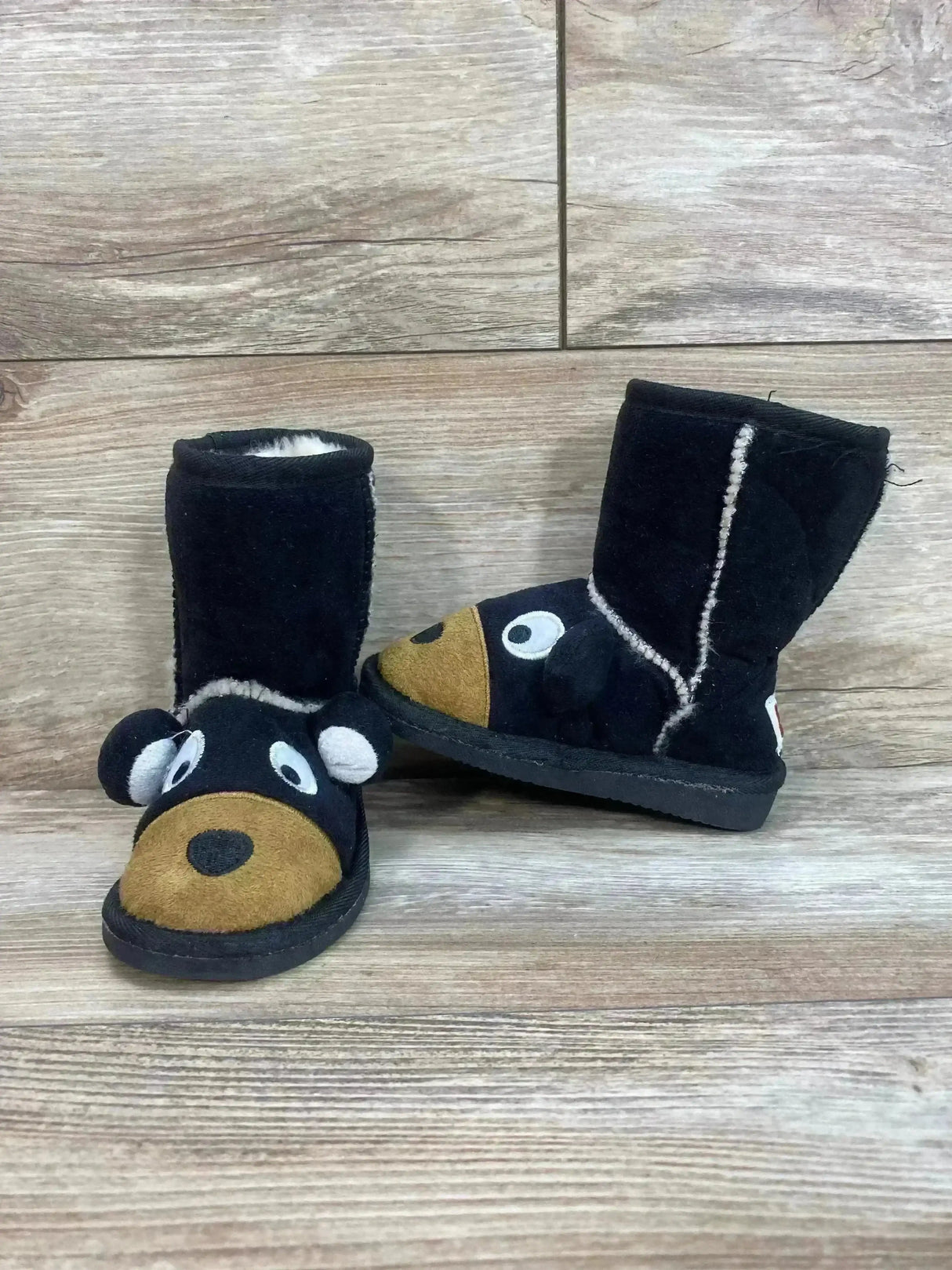 Angled view of black kids moose slipper boots with plush lining and brown moose face and ears on wood background