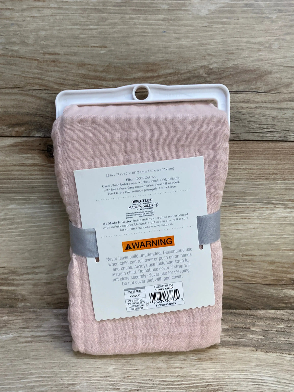 Front view of folded Cloud Island pink muslin changing pad cover showing WARNING label and OEKO‑TEX tag on wood background