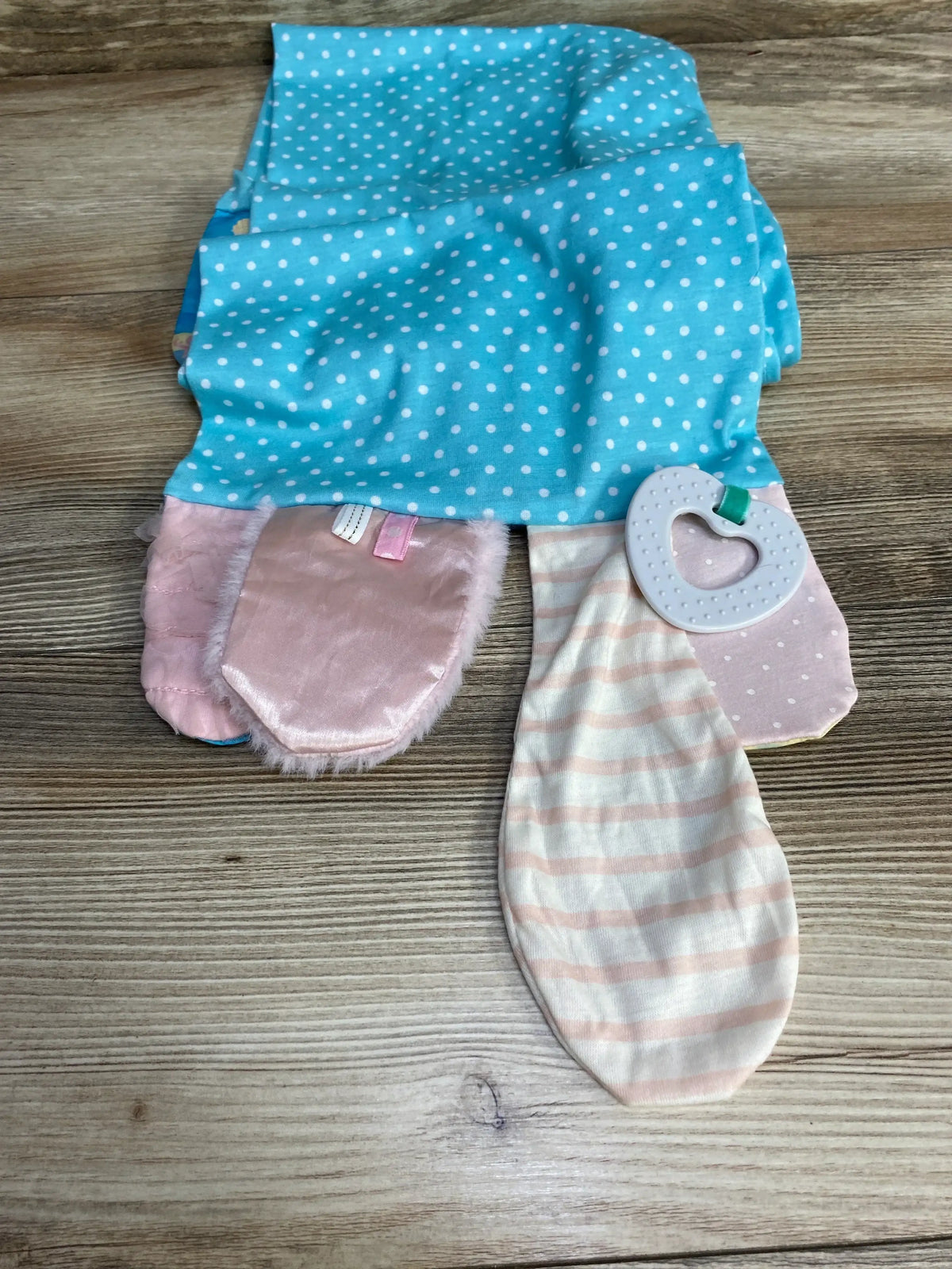 Top view of activity scarf for Mommy & Me (mermaid) showing turquoise polka-dot fabric, pink plush tag flaps and heart teether on wood