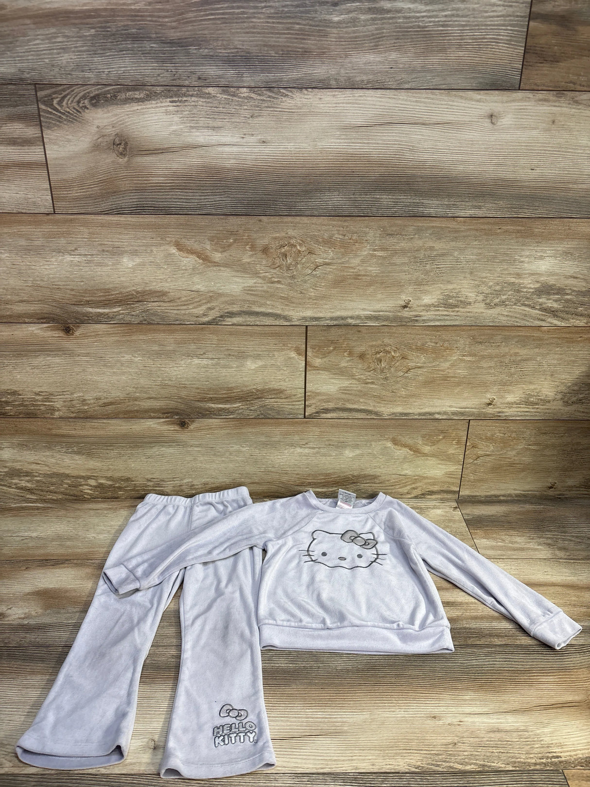 Flat lay of lilac Hello Kitty velour sweatshirt and pants size 4T showing front graphic and pant logo on wood backdrop
